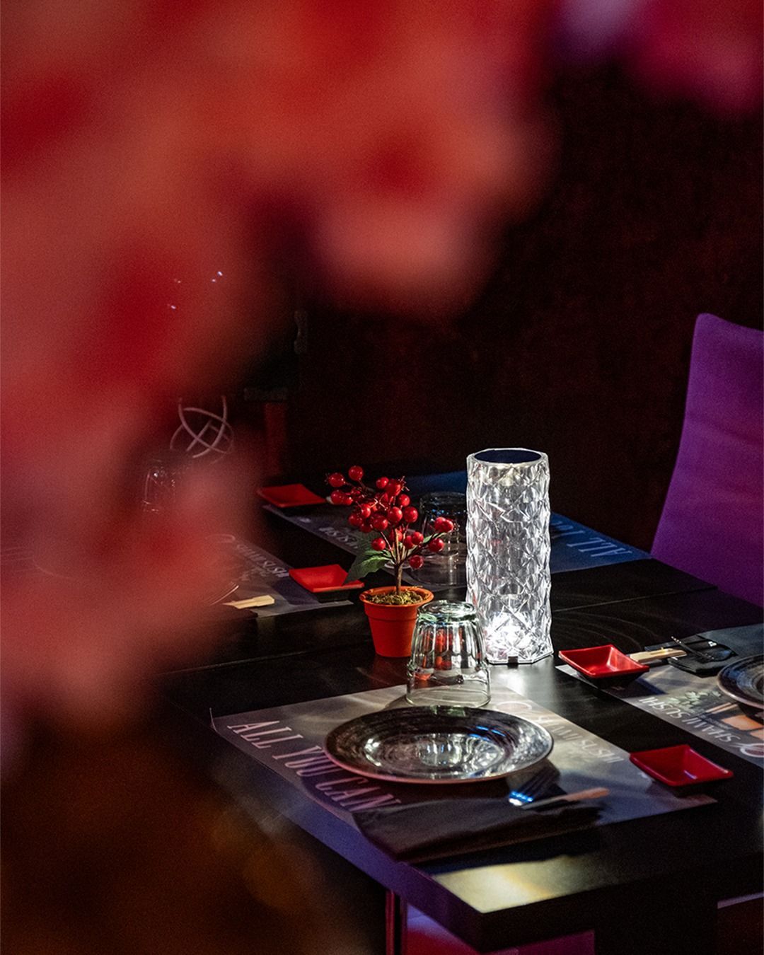 Apparecchiatura del tavolo del ristorante con lampada di cristallo, bacche rosse e posate. Atmosfera scura.