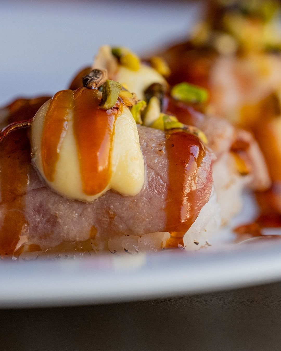 Sushi guarnito con guarnizione bianca, pistacchi e un filo di salsa su un piatto bianco.