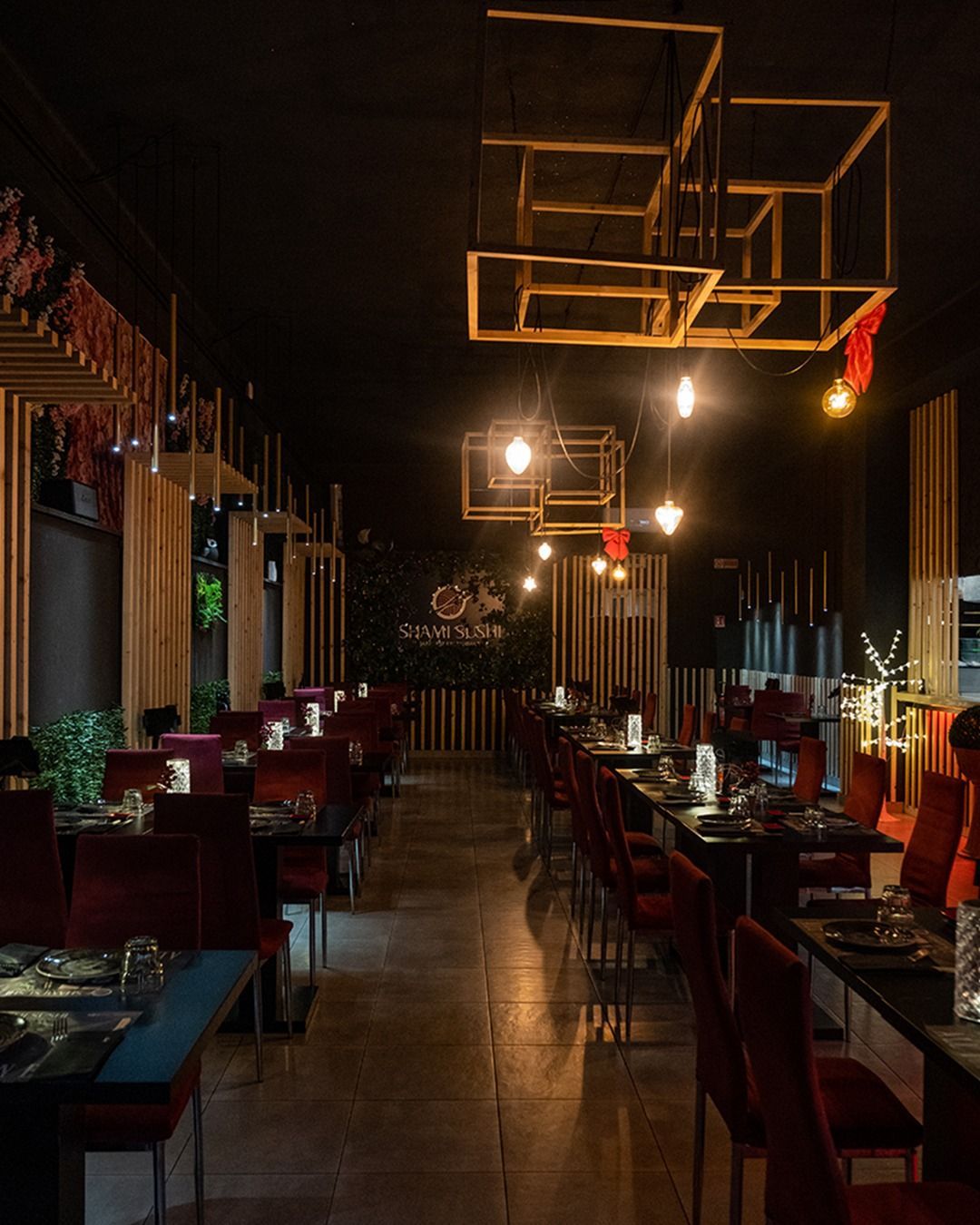 Interno del ristorante con sedie in velluto rosso, tavoli neri, dettagli in legno e luci geometriche sospese.