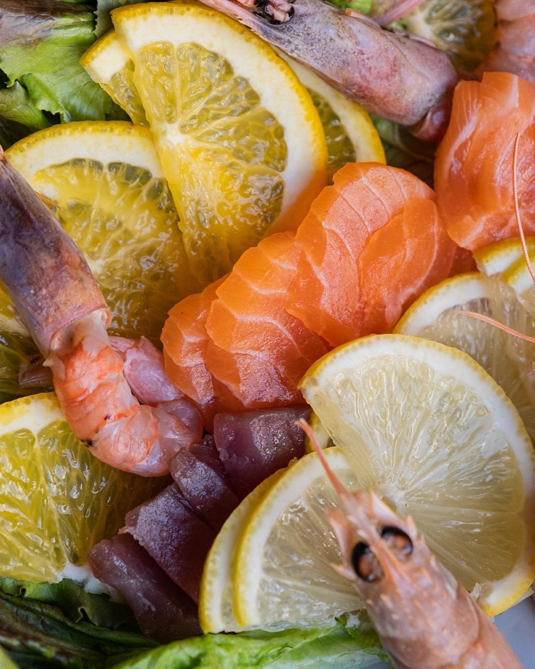 Fette di salmone, tonno, gamberi e agrumi su un letto di verdure.