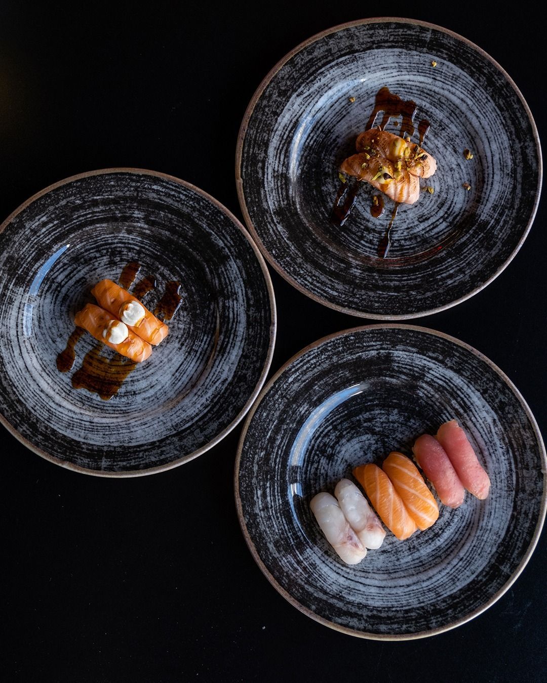 Piatti di sushi su piatti neri, disposti su una superficie scura.