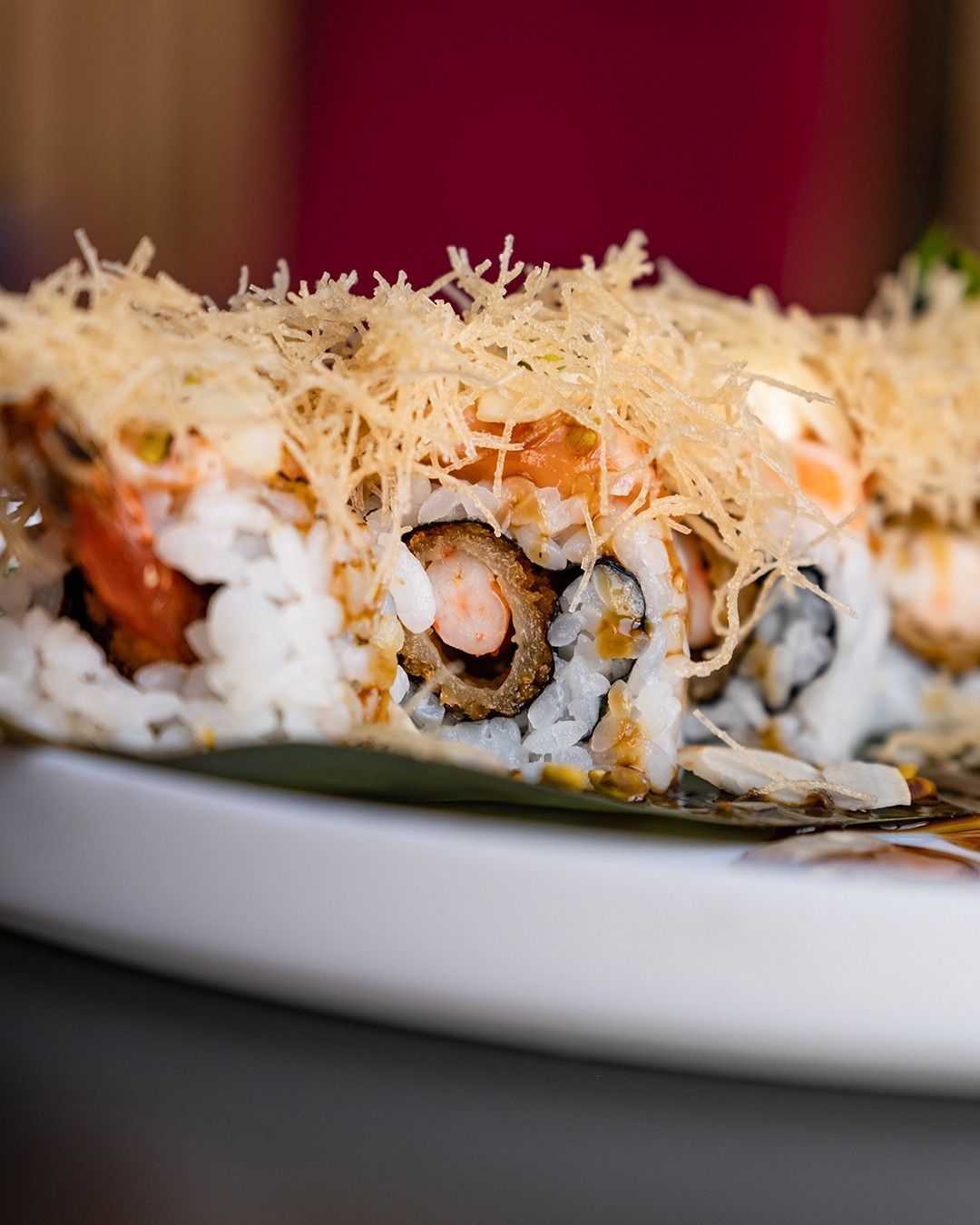 Rotolo di sushi con tempura e guarnizione sfilacciata, su un piatto bianco.