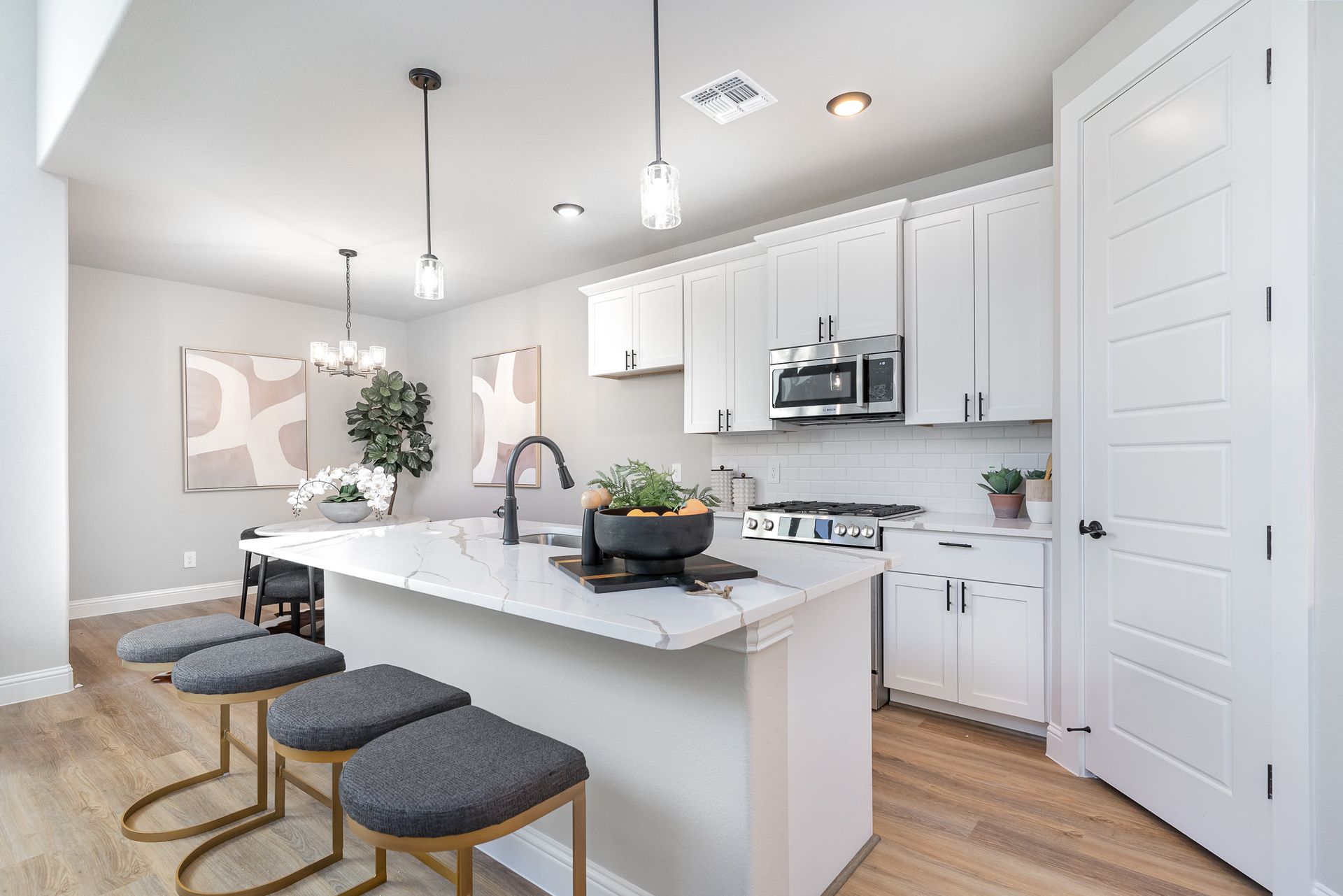 A kitchen with white cabinets and stools and a large island.