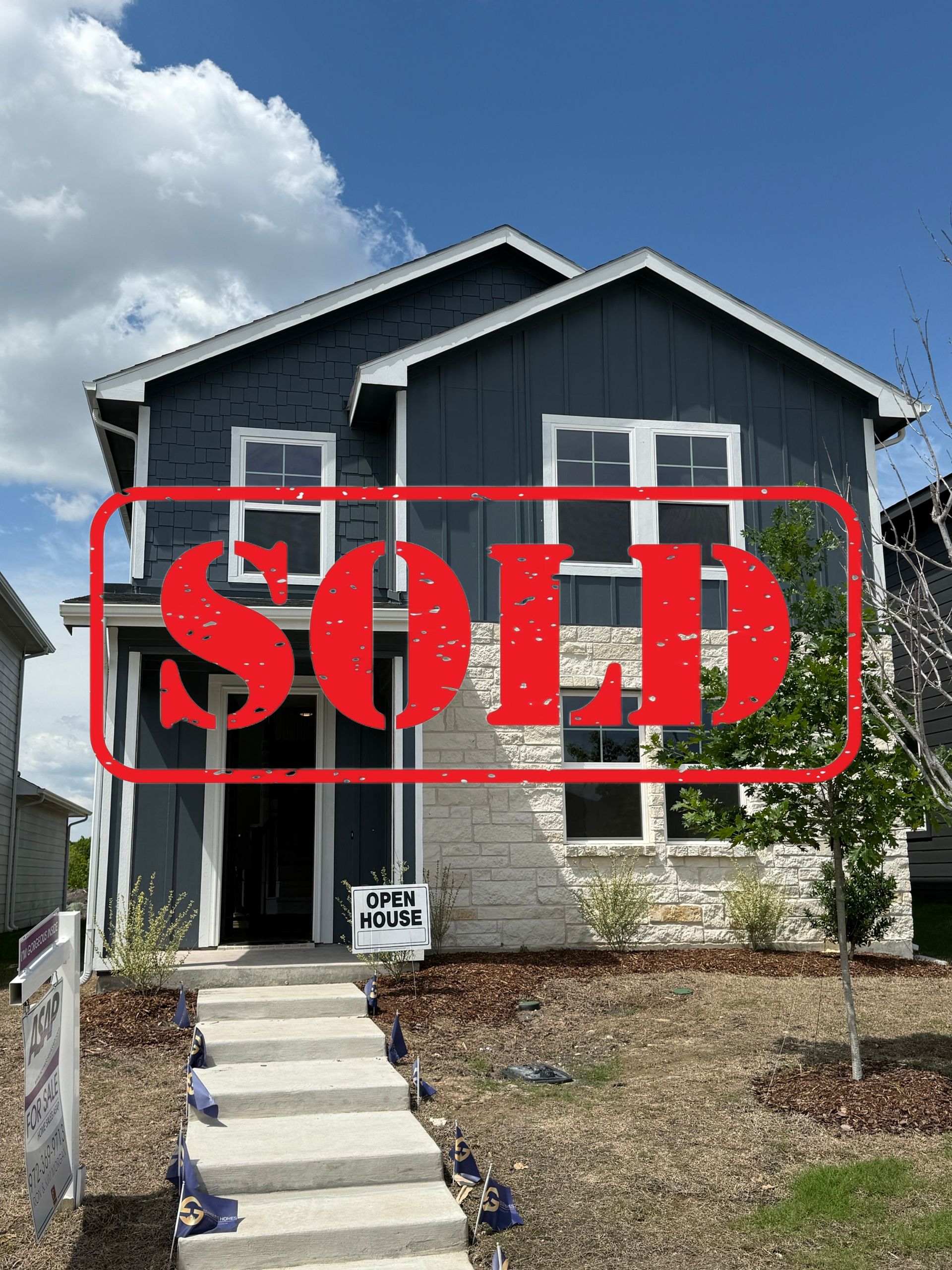 A white house with a black roof is sitting on top of a lush green field.