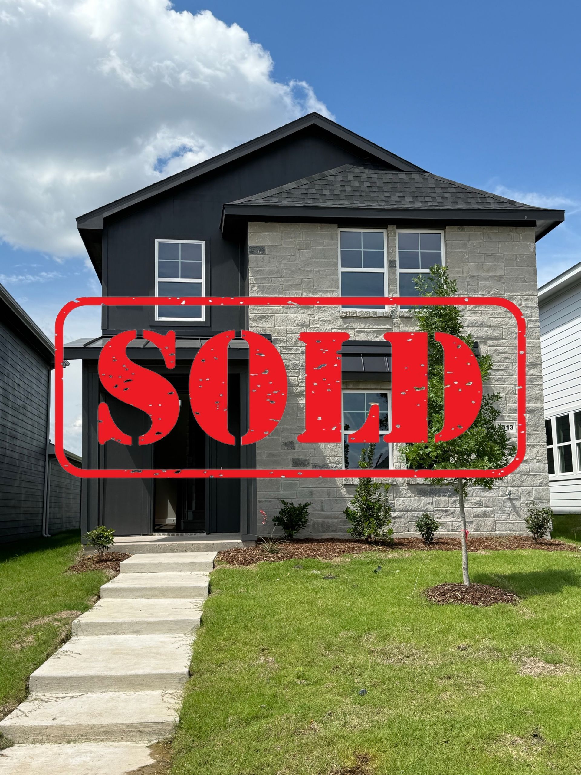 A white house with a black roof is sitting on top of a lush green field.