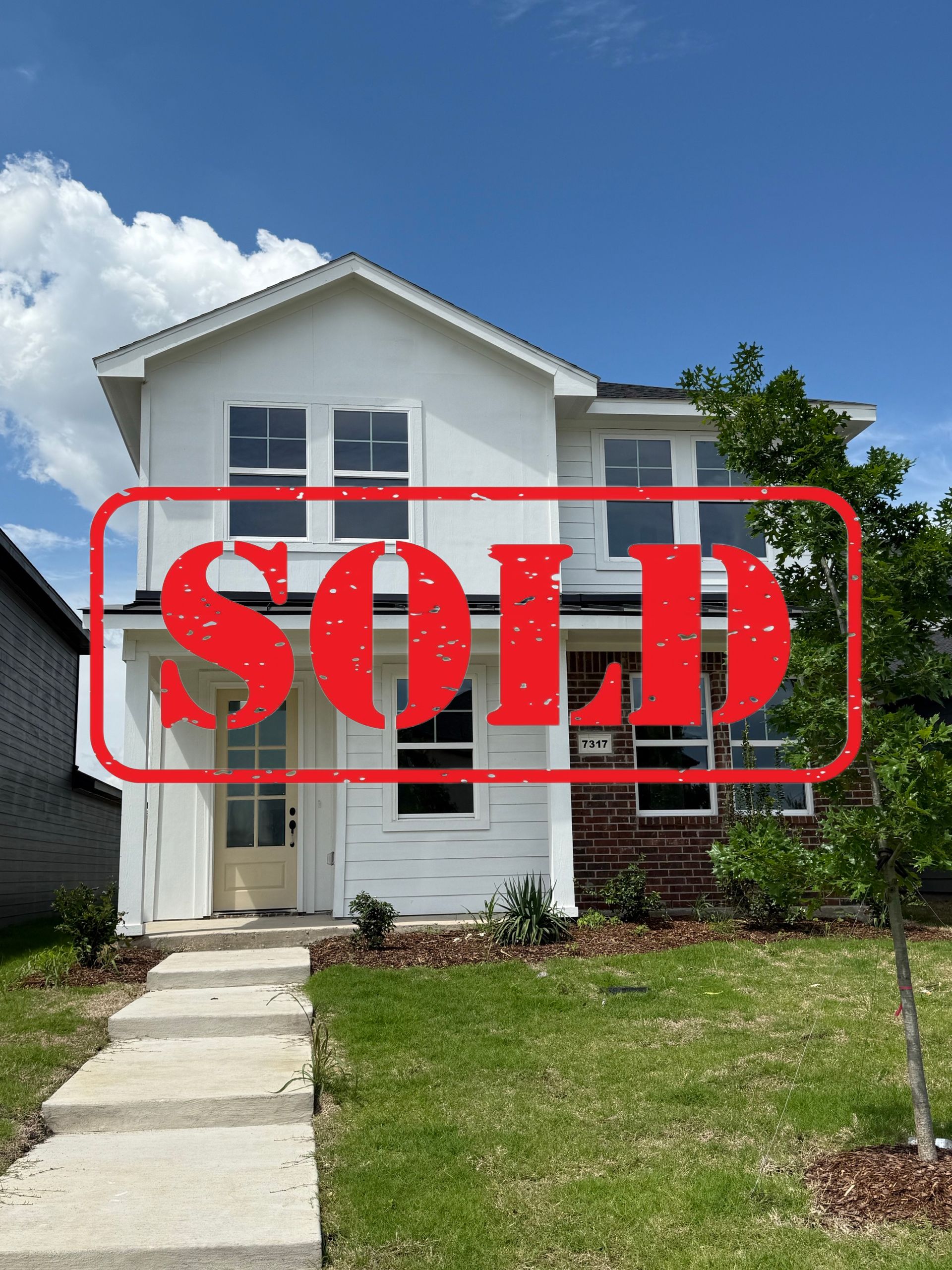 A white house with a black roof is sitting on top of a lush green field.