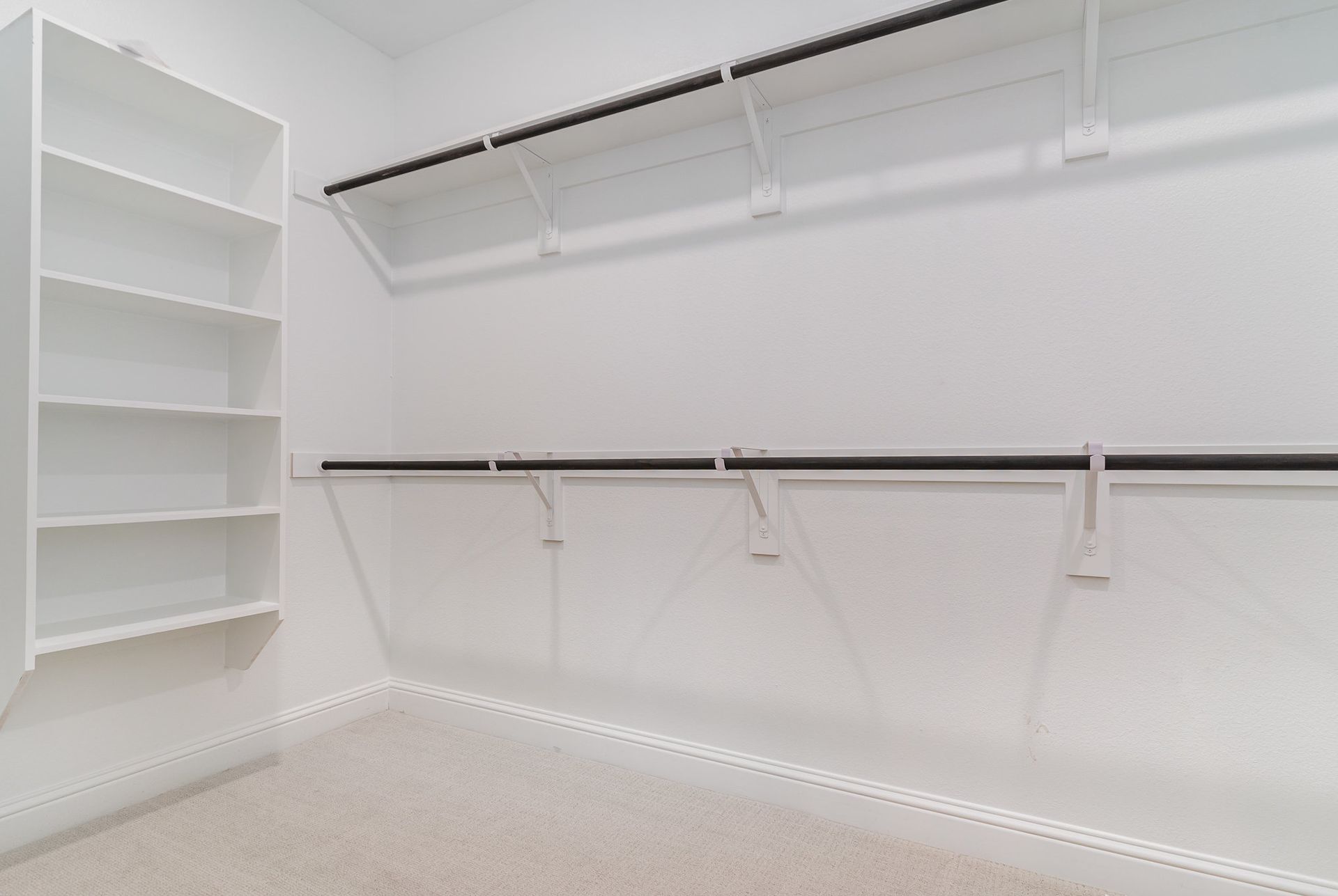 An empty walk in closet with white shelves and hanging racks.