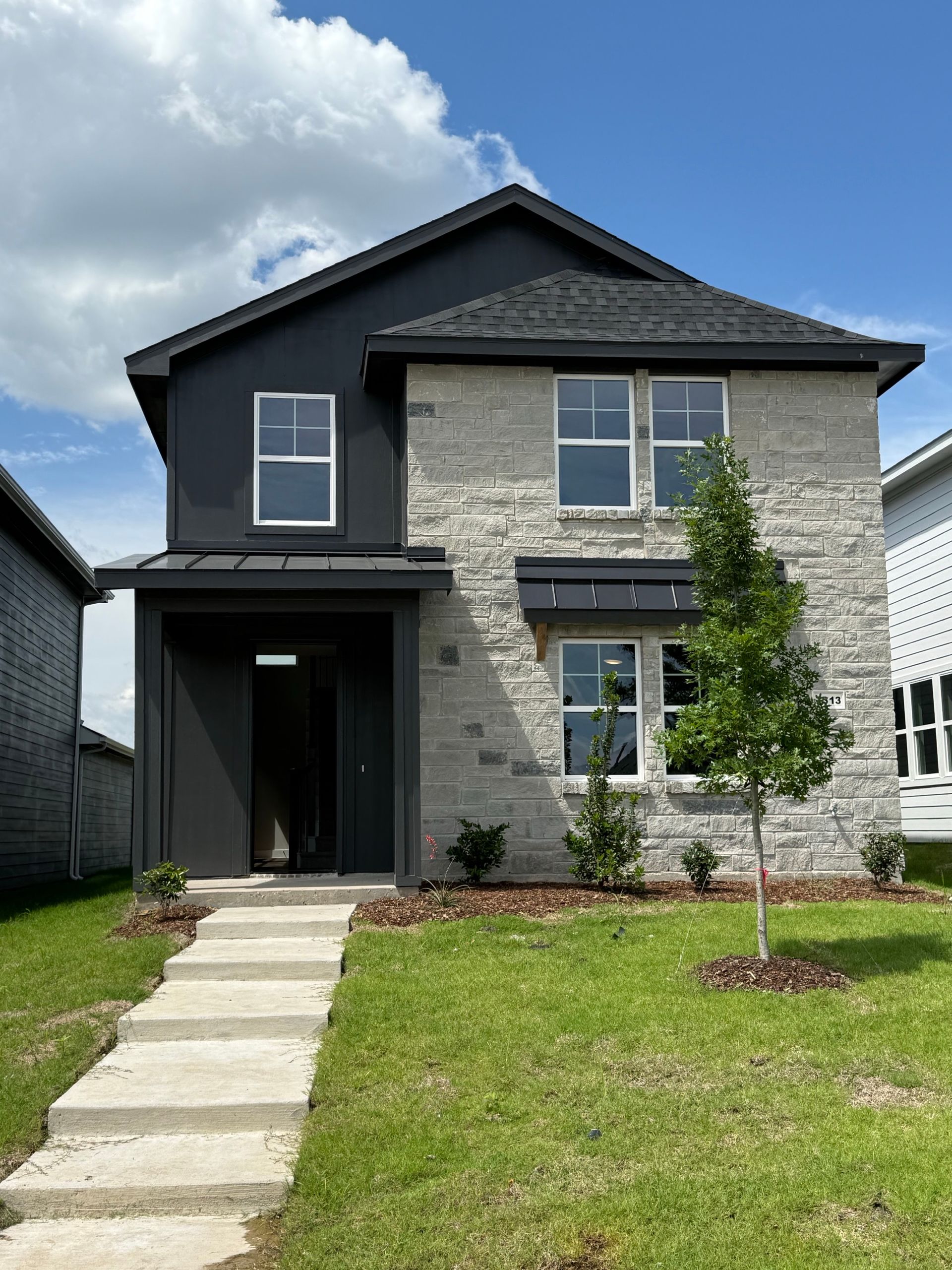 A white house with a black roof is sitting on top of a lush green field.