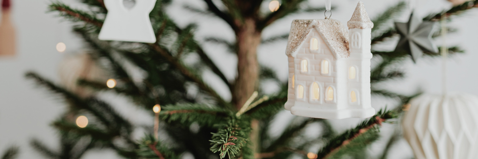 White ceramic house ornament hanging in a Christmas tree