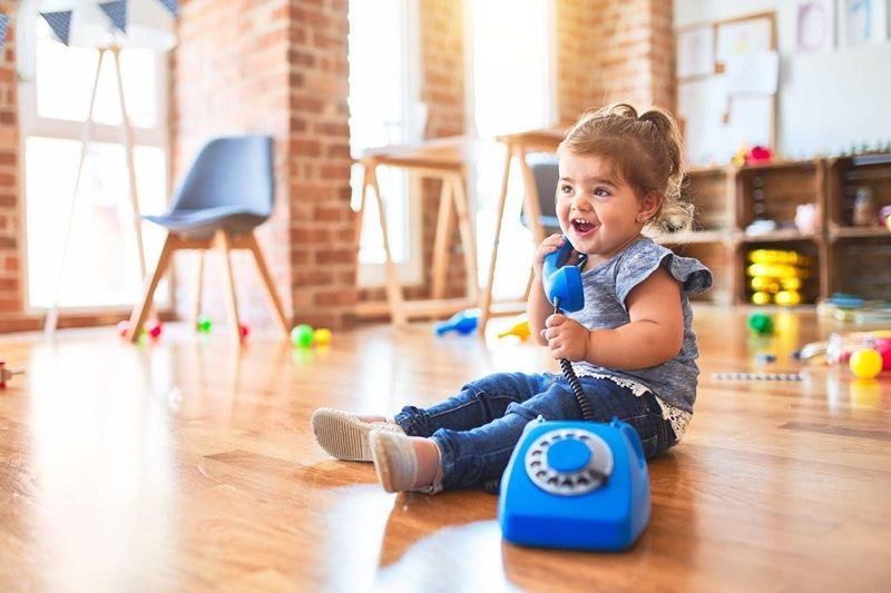 A young girl is sitting on a wooden floor and is playing with a toy telephone.