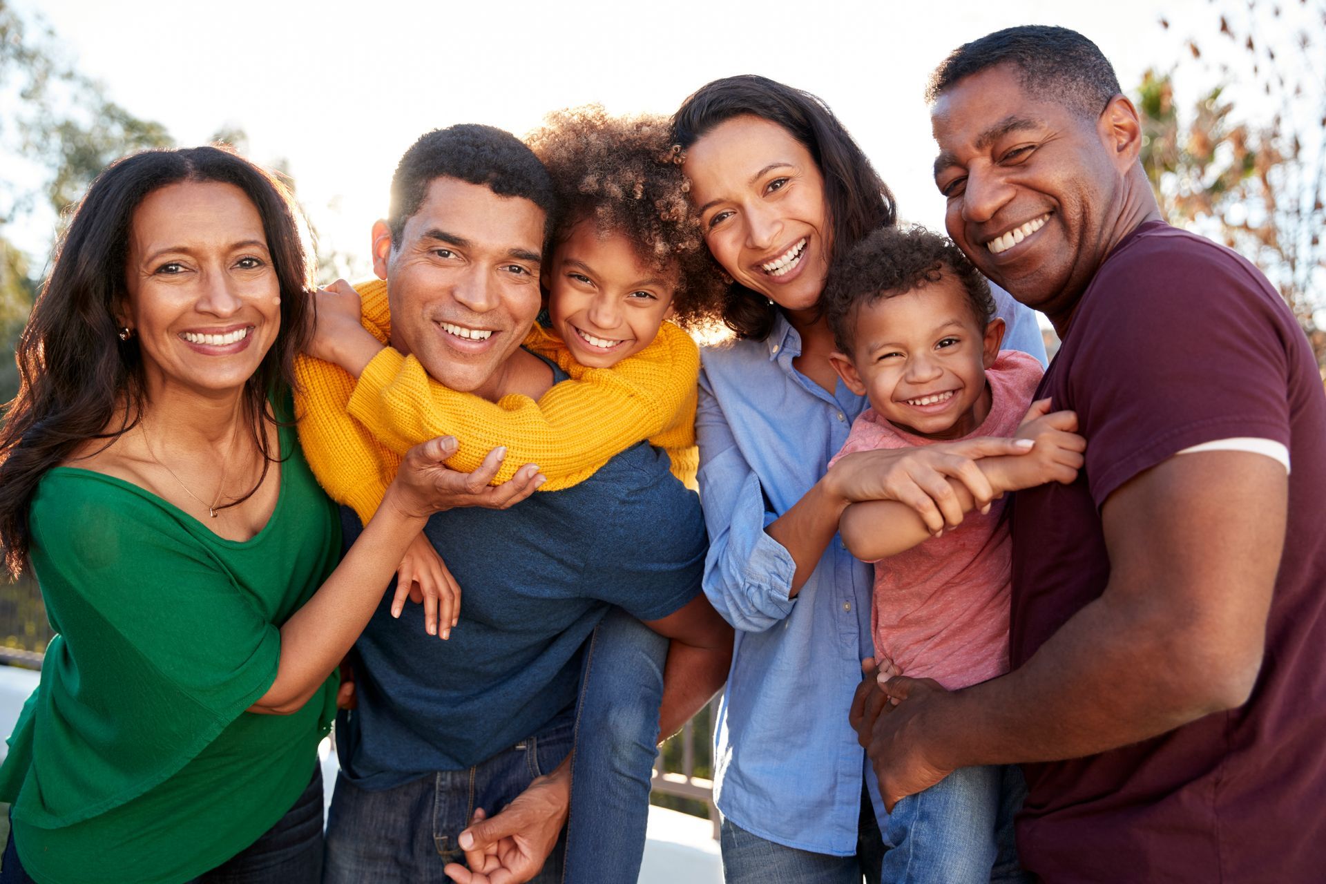 A family of children and adults in bright clothing are standing outside smiling.
