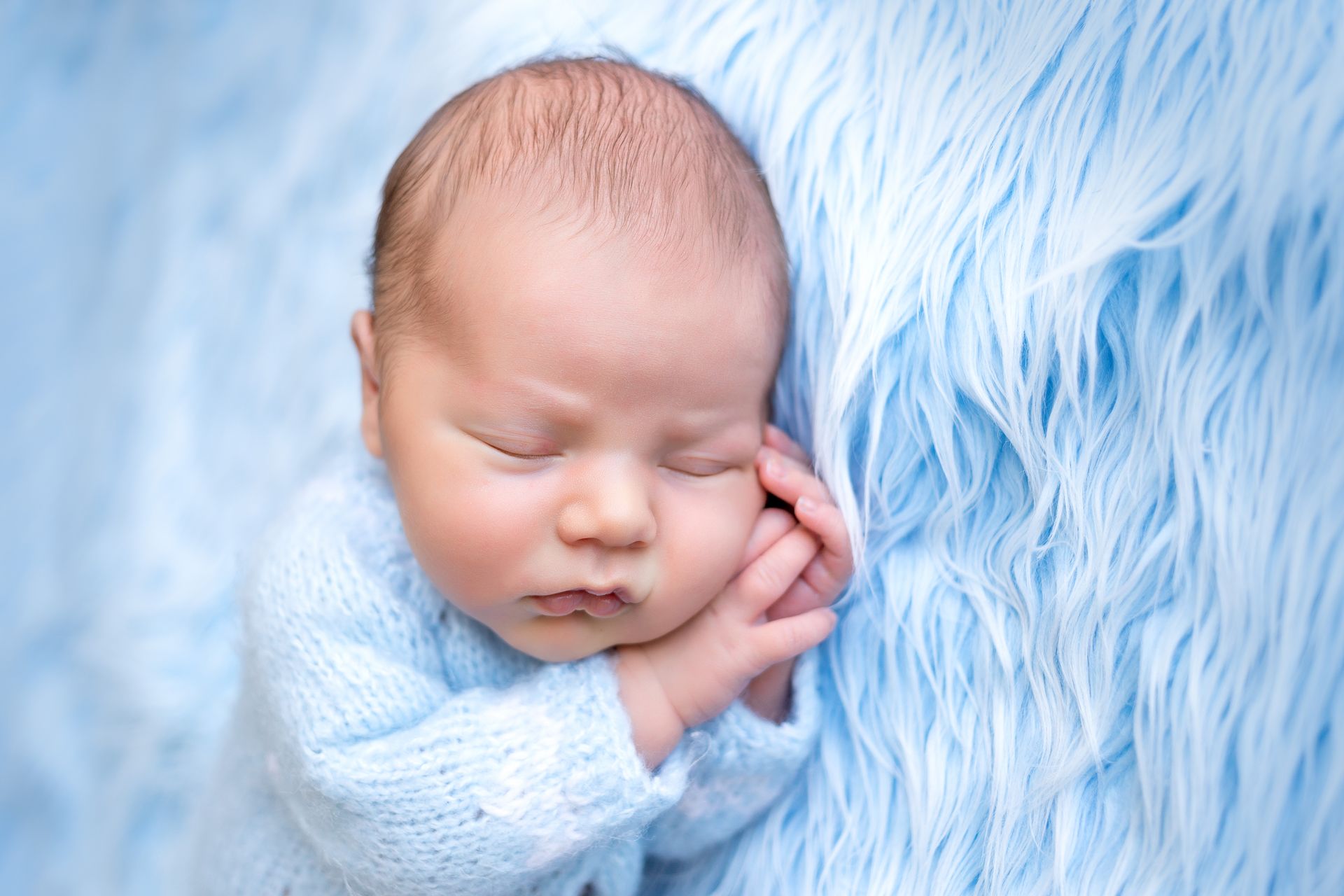 A sleeping newborn baby in a blue sweater. Grandville Pediatrics cares for children, from newborn through early adult.