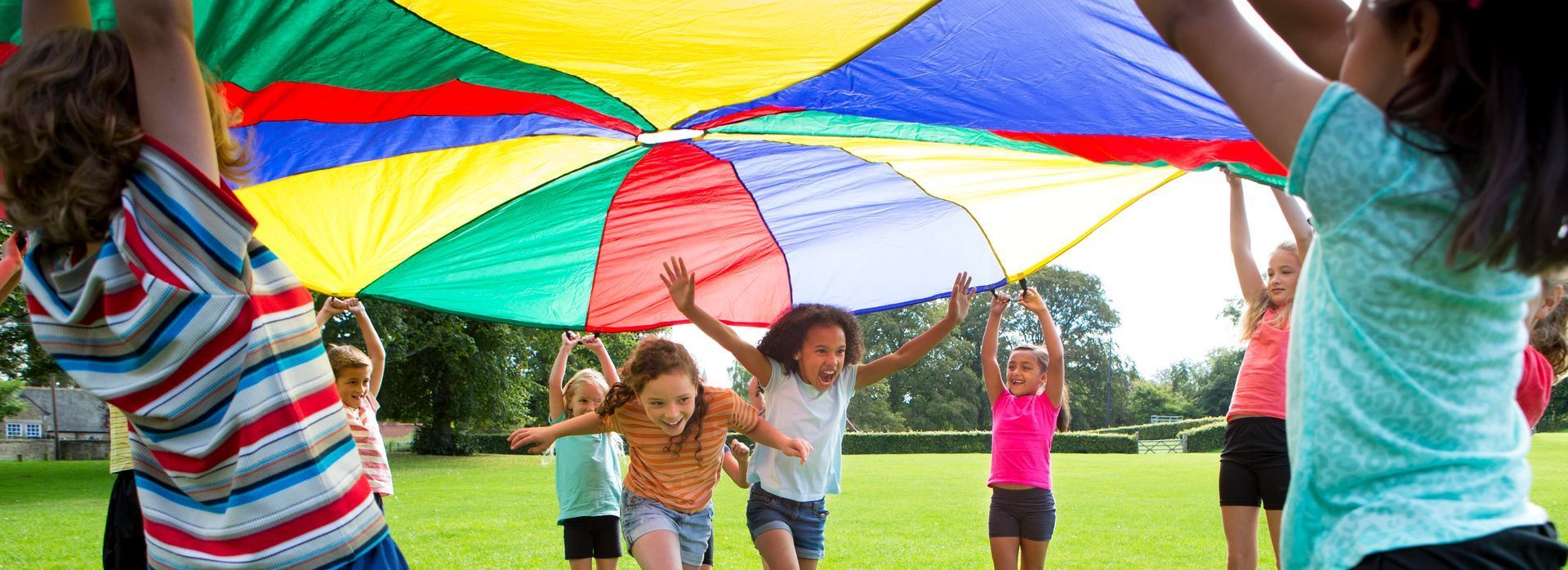 Children running under a colorful sheet in the park.