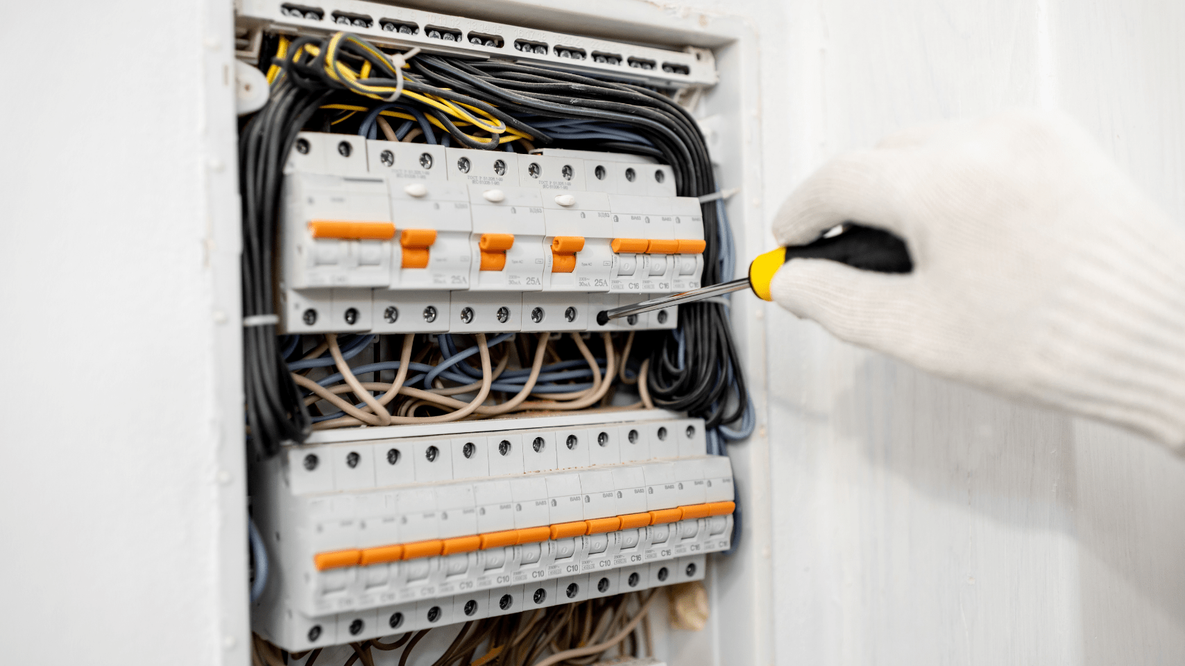 Hand in a white glove using a screwdriver in a circuit breaker box — Paul Wiedman Electrical in Harristown, QLD