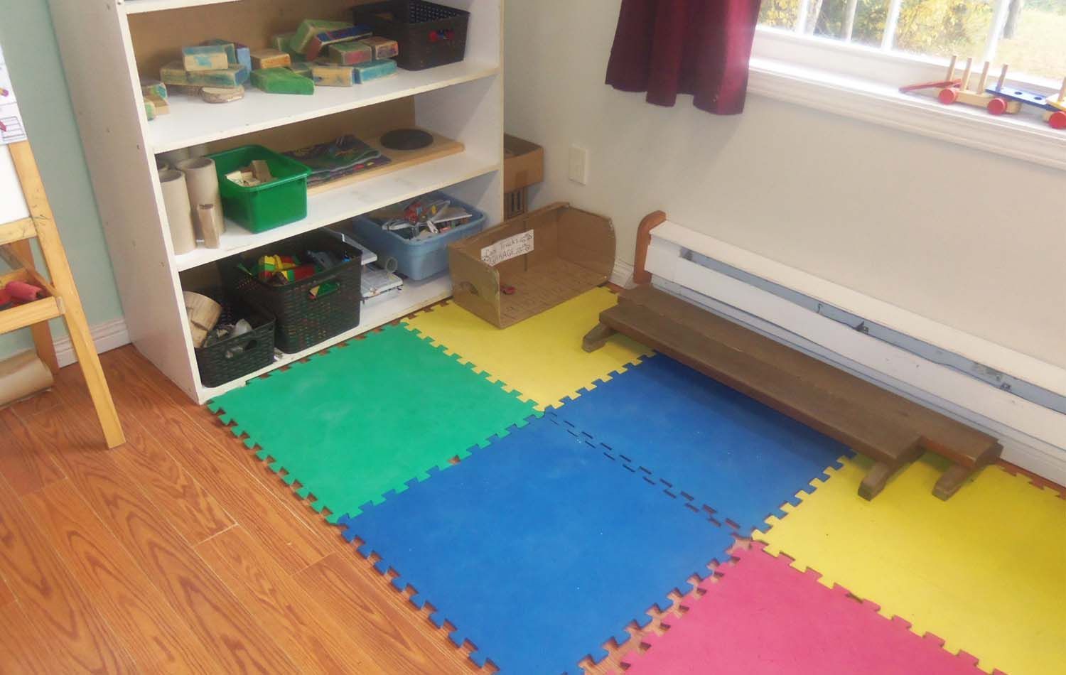 Playroom corner with colorful floor mats, a wooden bench, and a shelf filled with toys.