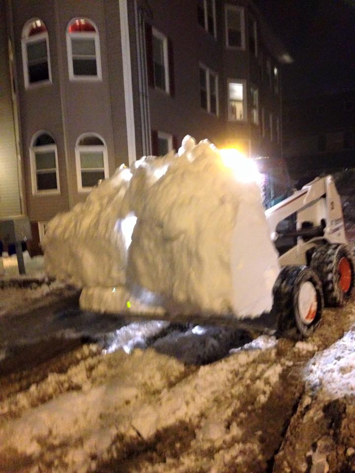 A bobcat is clearing snow from a driveway at night