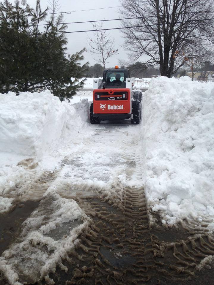 A bobcat snow plow is clearing snow from a driveway