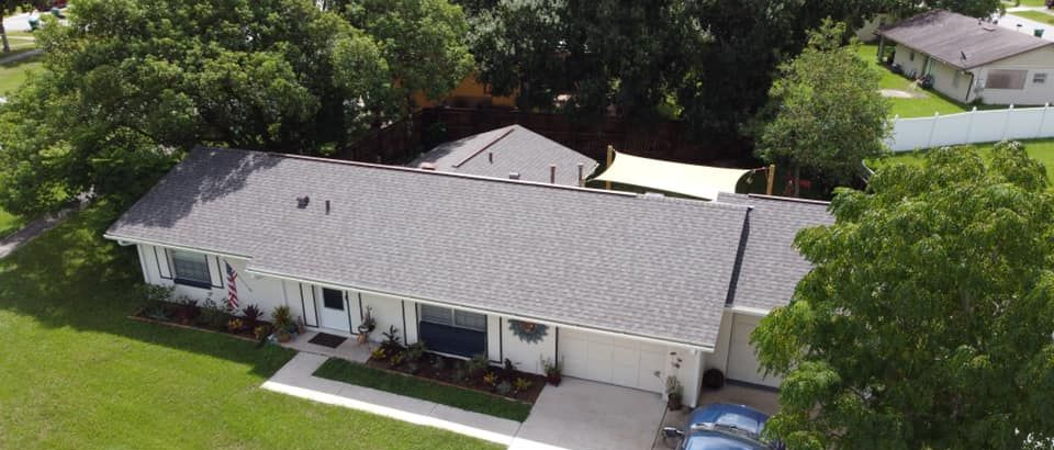 Aerial view of a single-story white house with a gray roof, green lawn, and trees surrounding it.