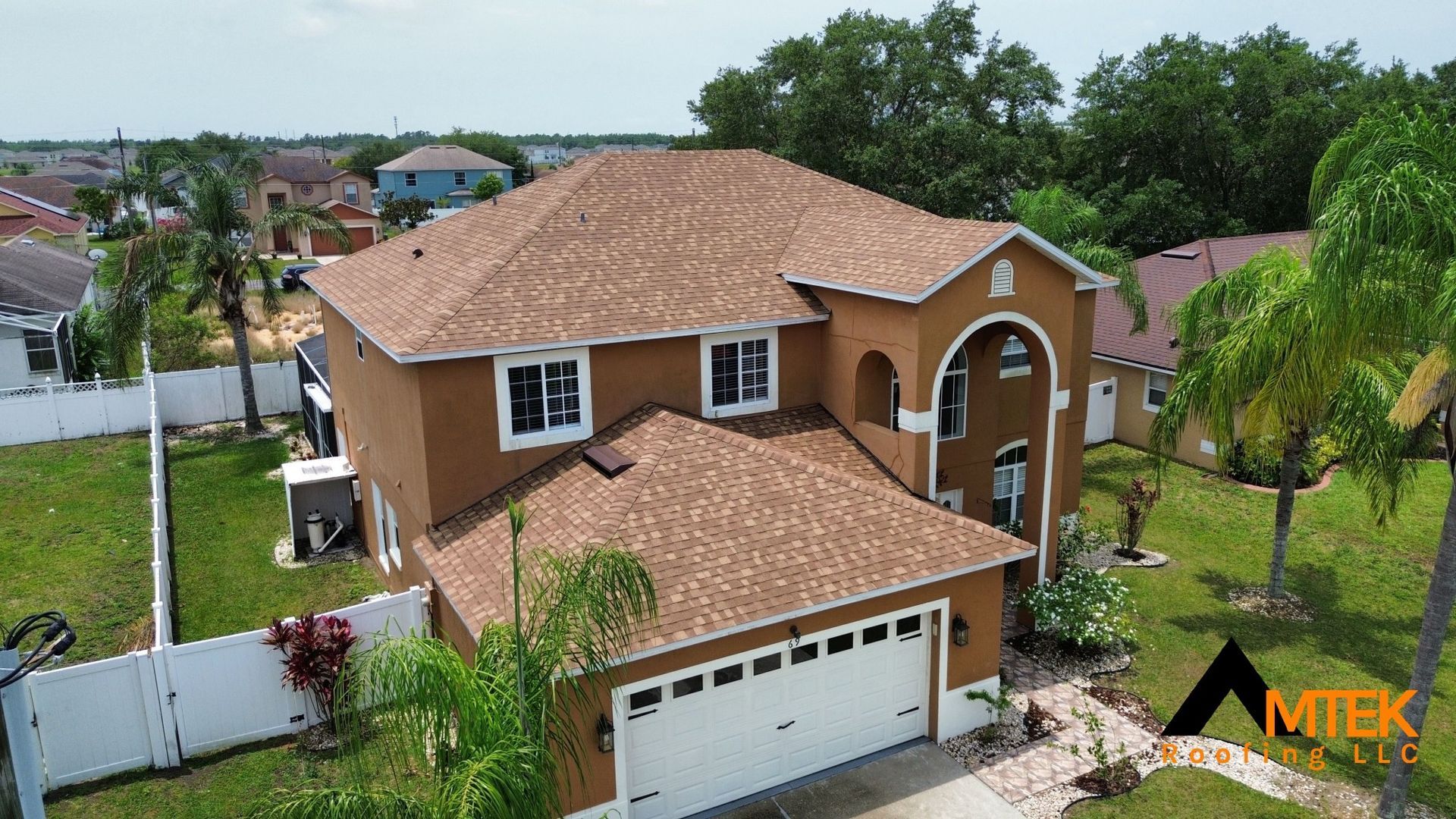 Two-story tan house with a red-tile roof, white garage, and landscaped yard in a suburban neighborhood