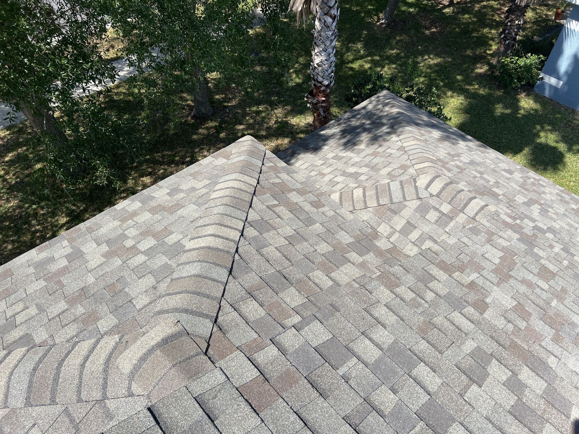 Worker in red shirt repairing shingles on a roof with tools and safety harness