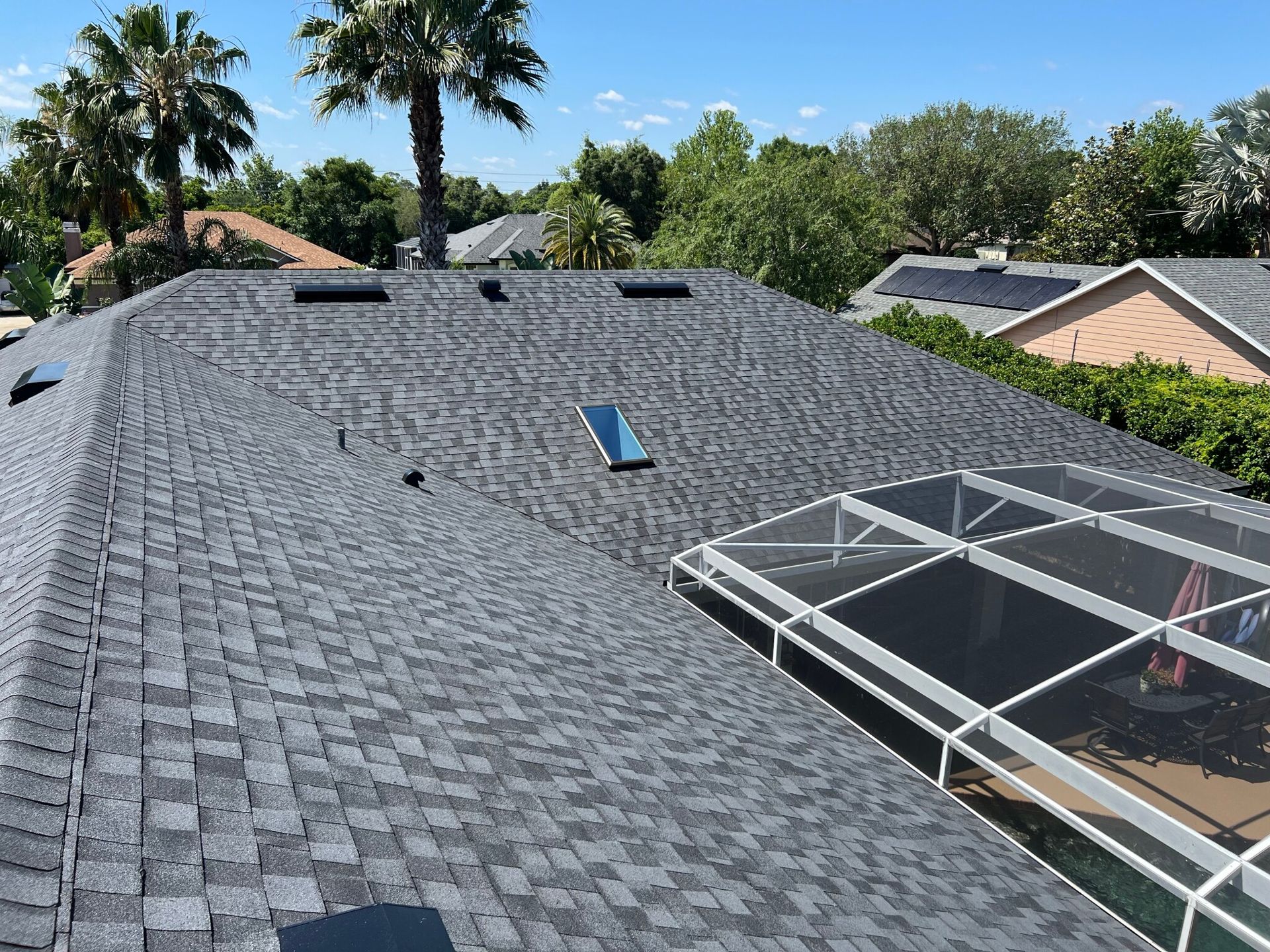 Gray shingled roof with skylights and solar panels, viewed from above with palm trees nearby