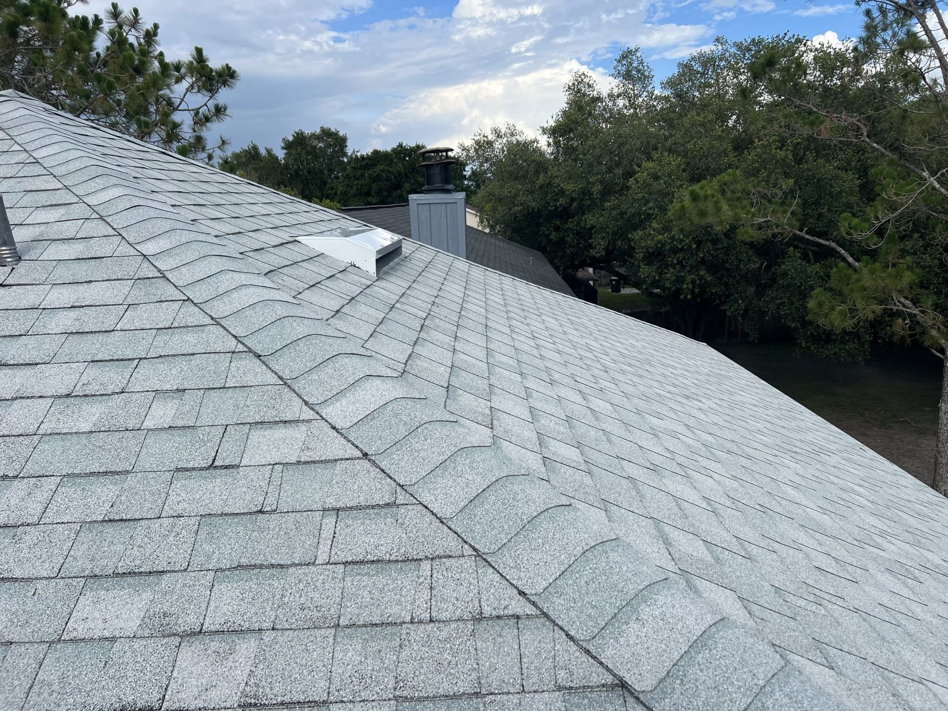 Worker stacking metal roofing sheets on a roof under a bright blue sky