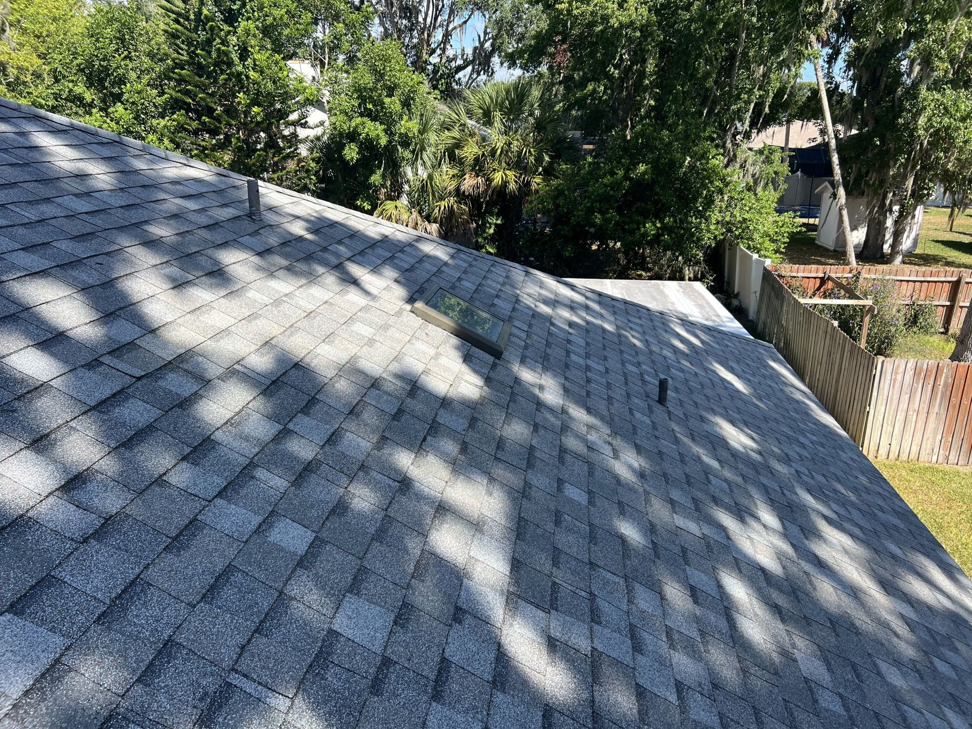 Gray shingled roof with tree shadows in bright daylight