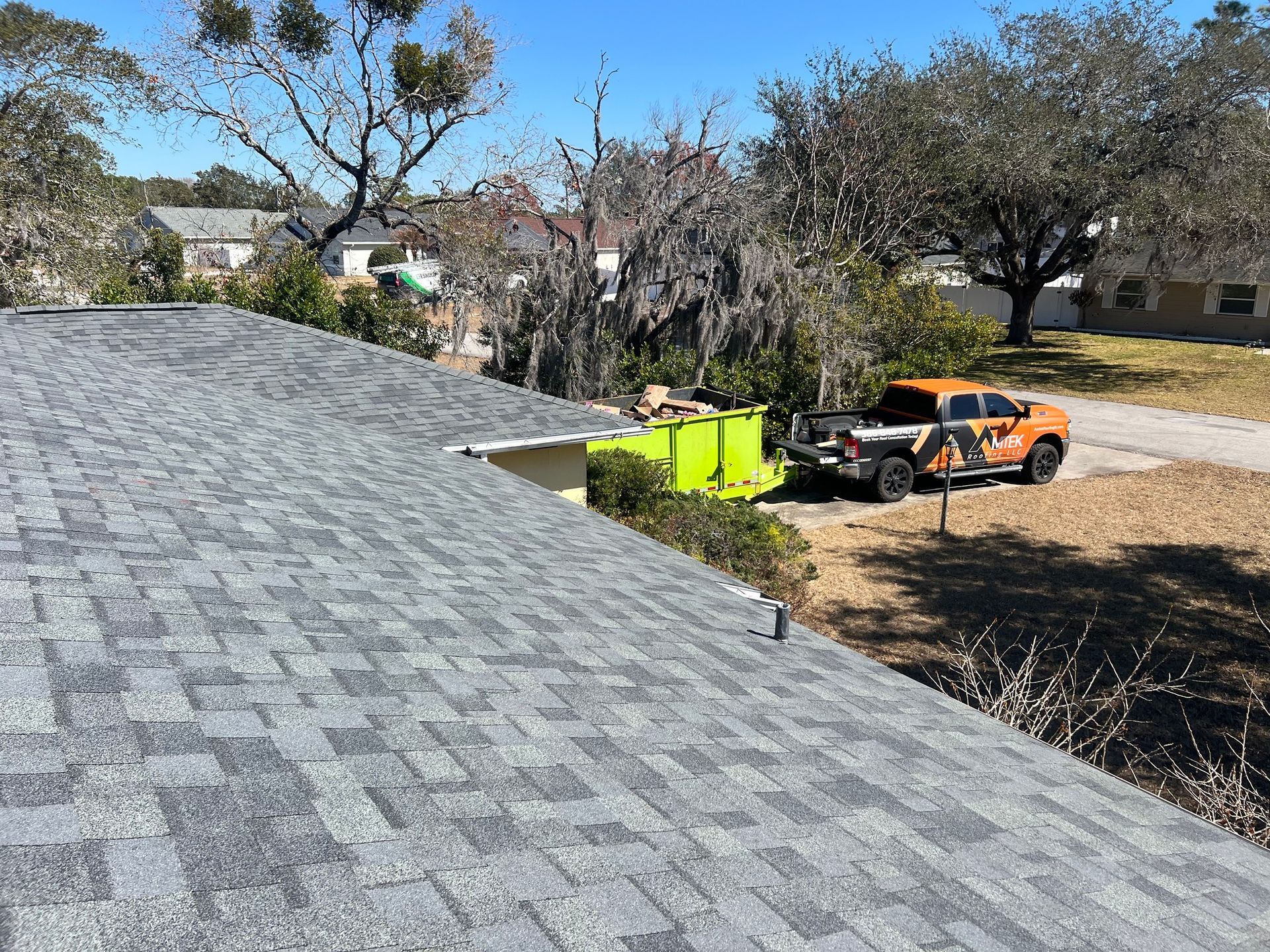 Workers on a roof near green bins and an orange utility vehicle in a suburban yard