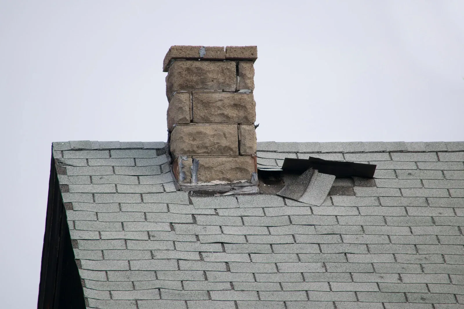 Damaged gray roof with a brick chimney and broken shingles