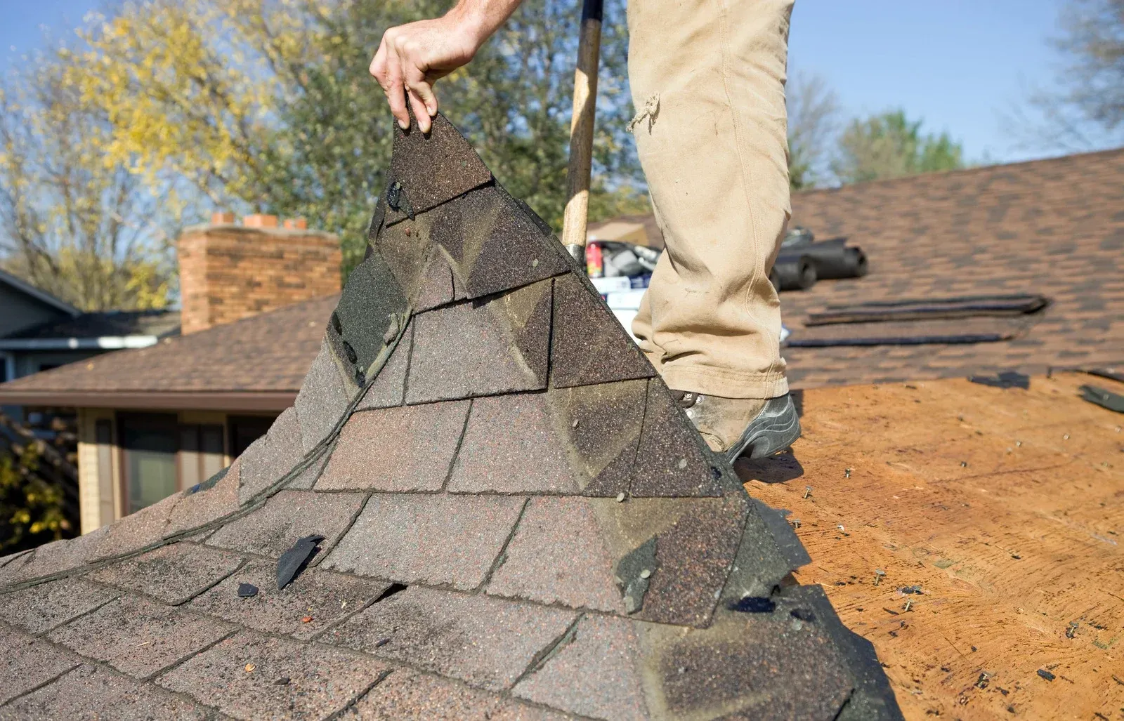 Aerial view of workers repairing a roof with orange and gray shingles beside a house and yard