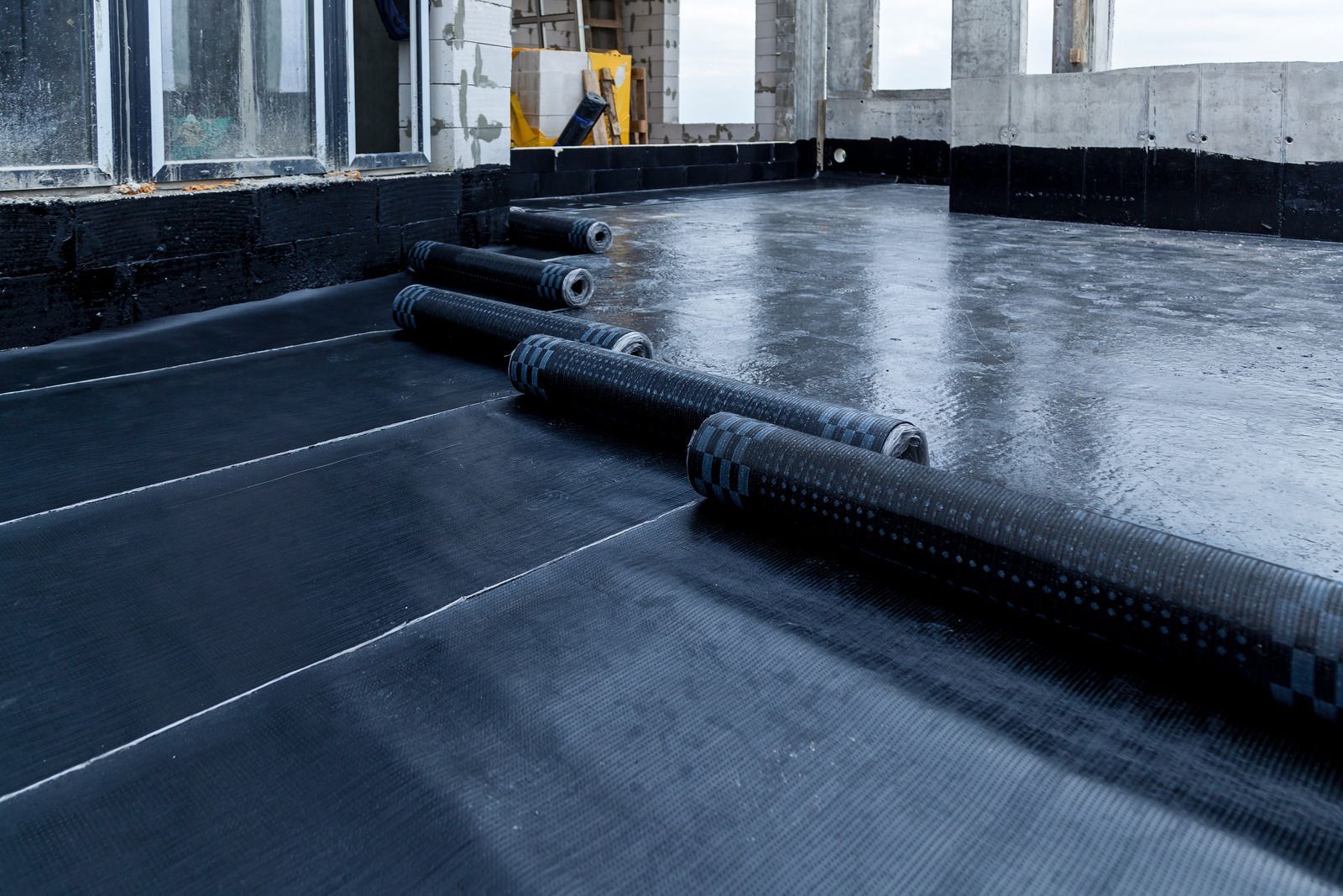 Black waterproof roofing membrane being installed on a flat roof during rainy weather