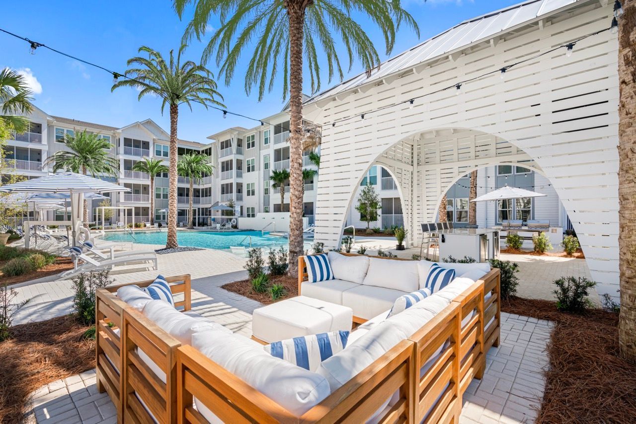 Outdoor pool area with white patio seating, palm trees, and string lights at a modern apartment community.