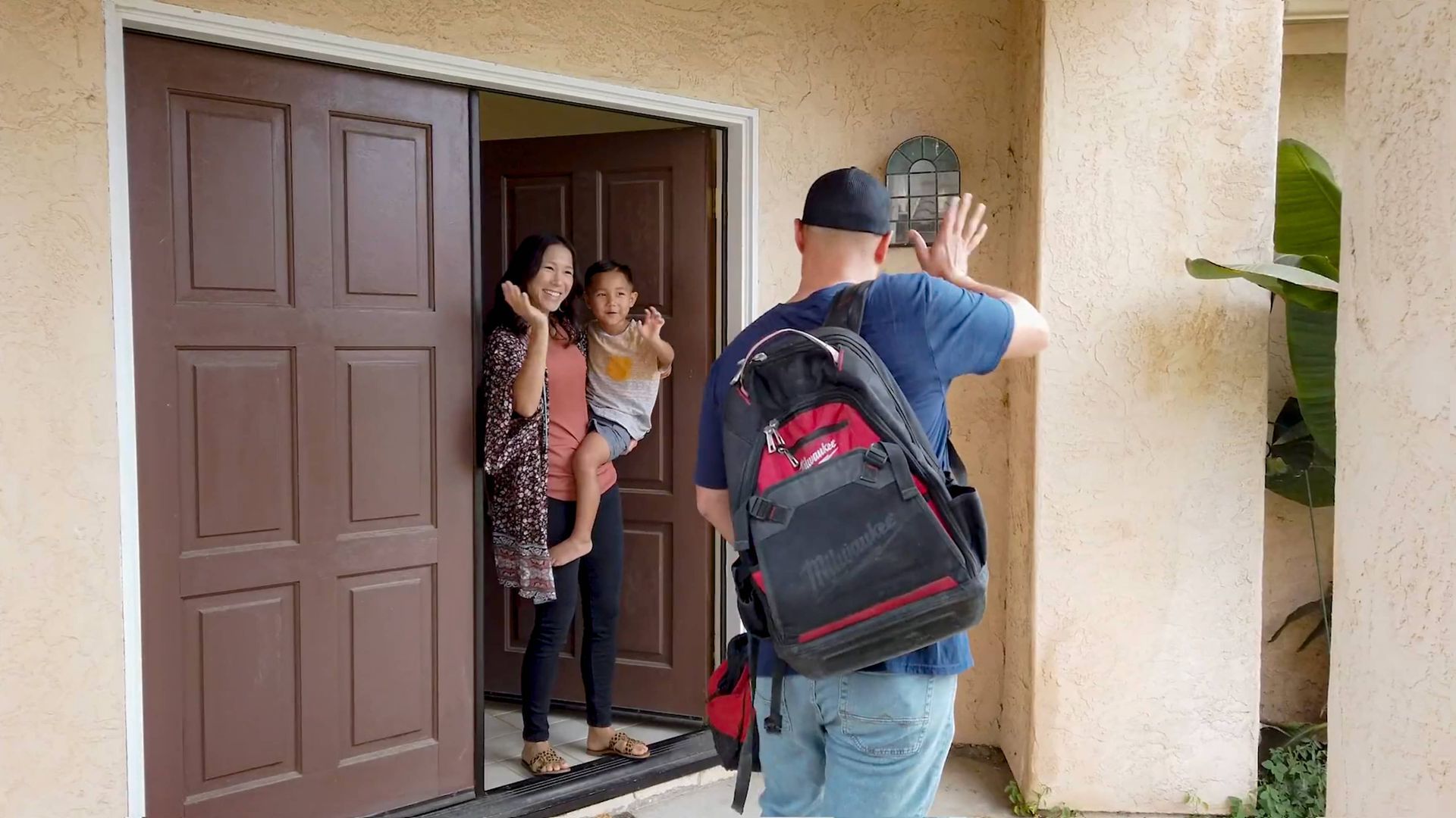 Man waving goodbye to woman and child at doorway. Woman holding child.