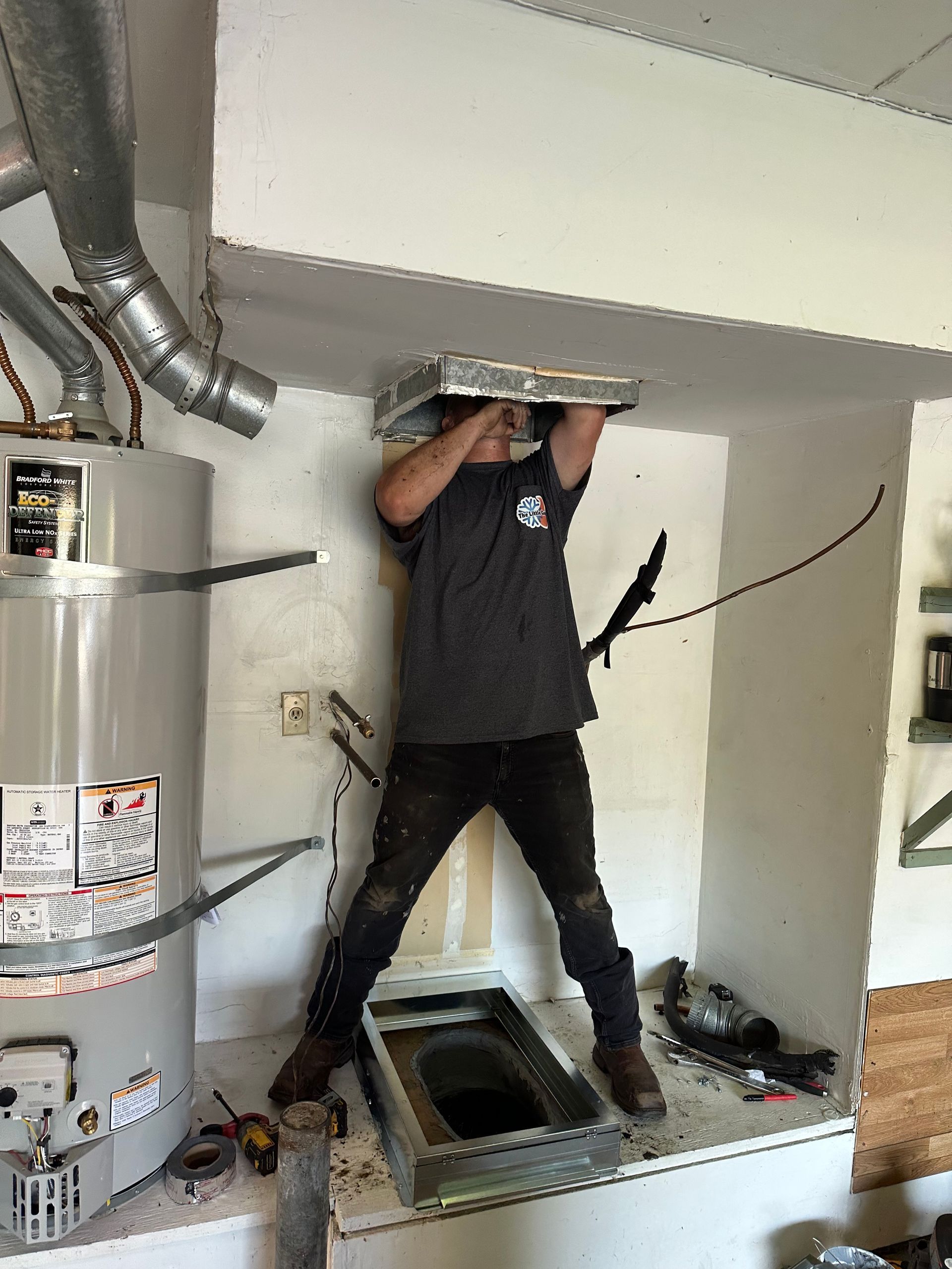A person installs ventilation near a water heater in an unfinished room.
