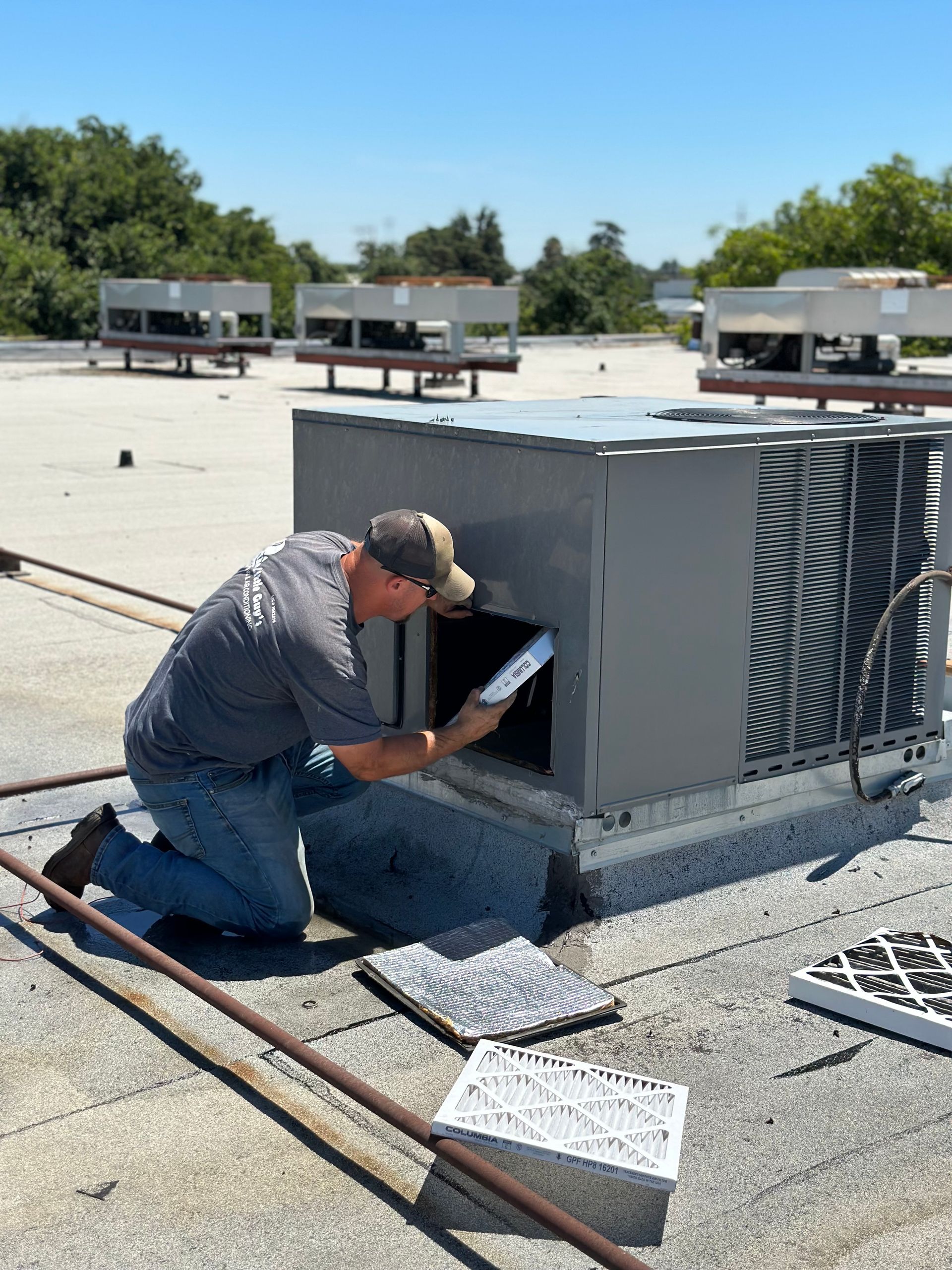 HVAC technician, on rooftop, servicing an air conditioning unit; blue sky, sunny day.