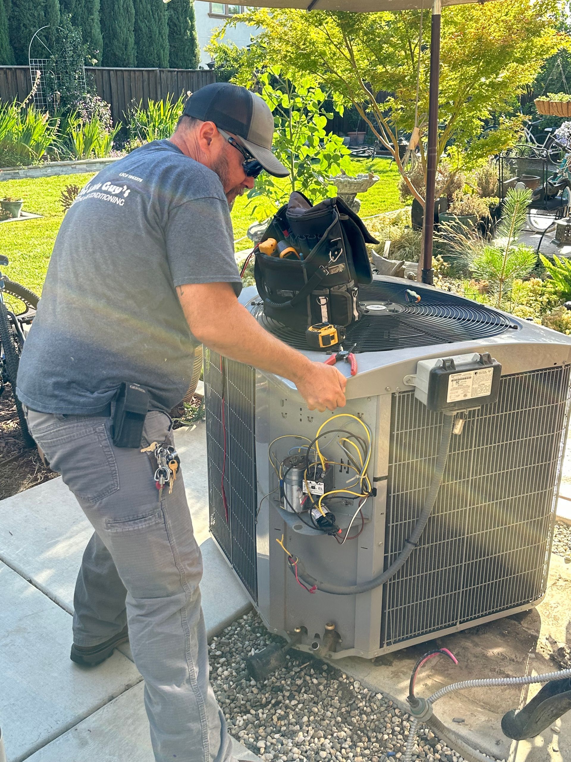 HVAC technician working on an outdoor air conditioning unit in a residential yard.