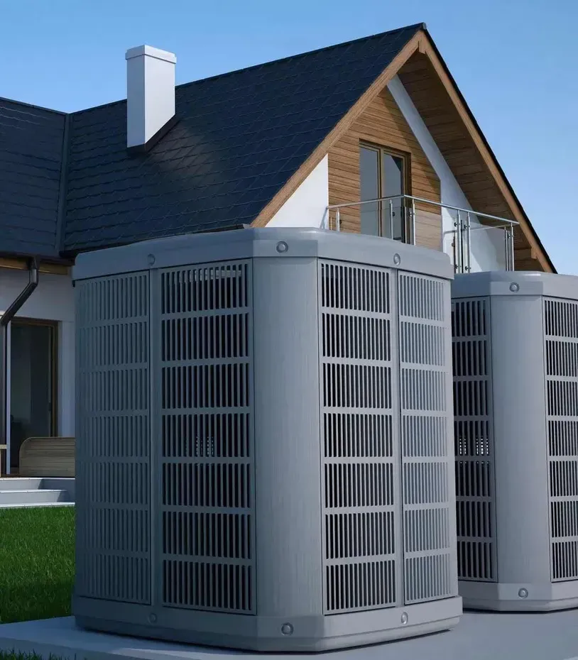 Two large gray air conditioning units in front of a house with a black roof and a white chimney.