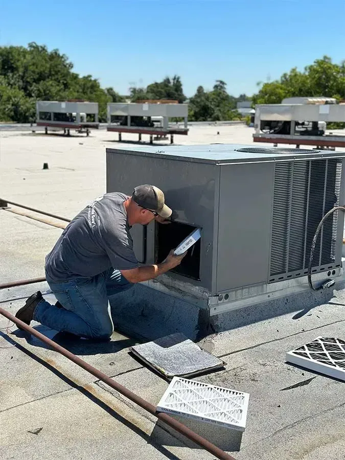 HVAC technician inspecting air filter on a rooftop unit on a sunny day.