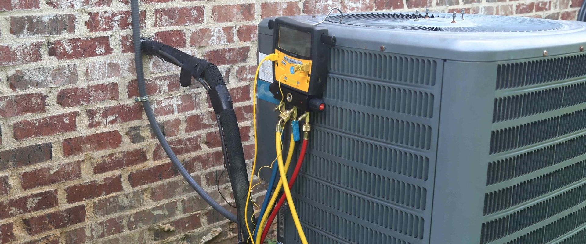 AC unit being serviced. Hoses are connected to a gauge on top of the unit by a brick wall.