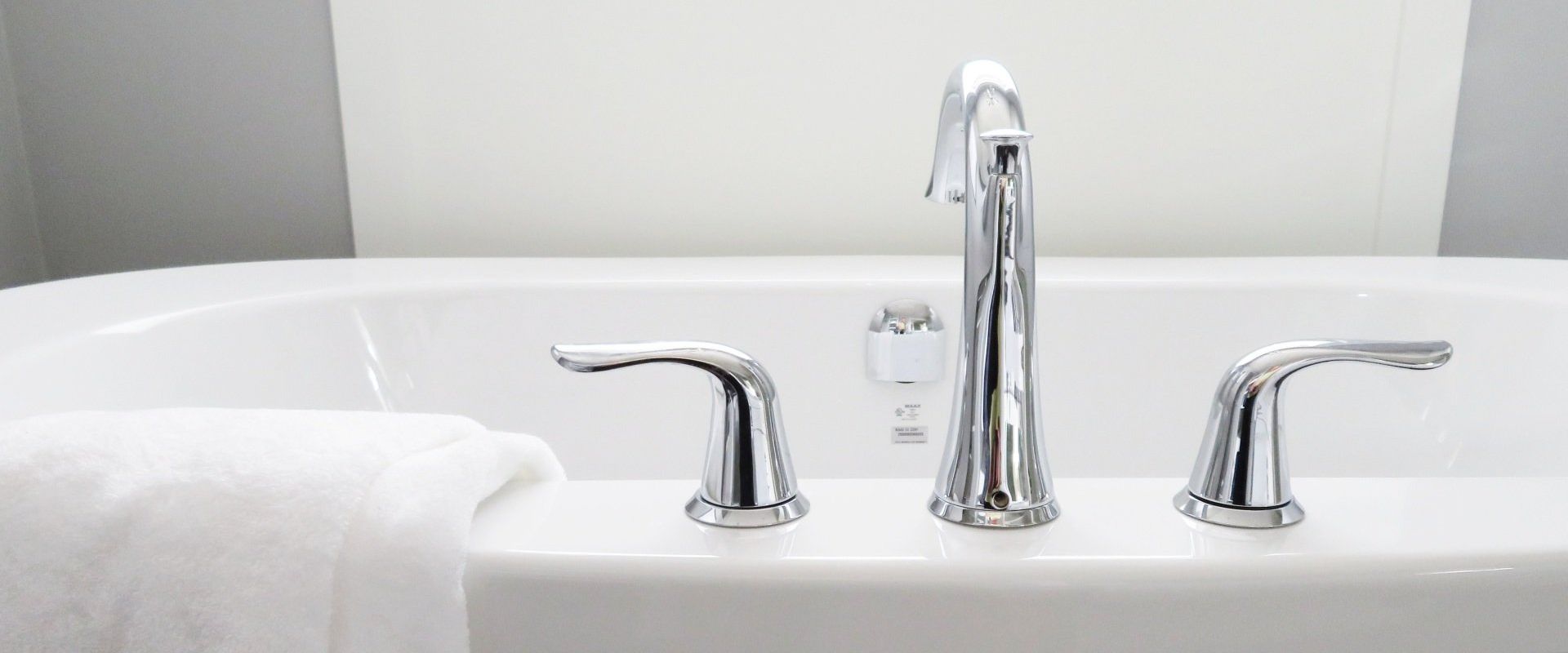 Close-up of a white bathtub with shiny chrome faucet and handles. A white towel is draped on the side.