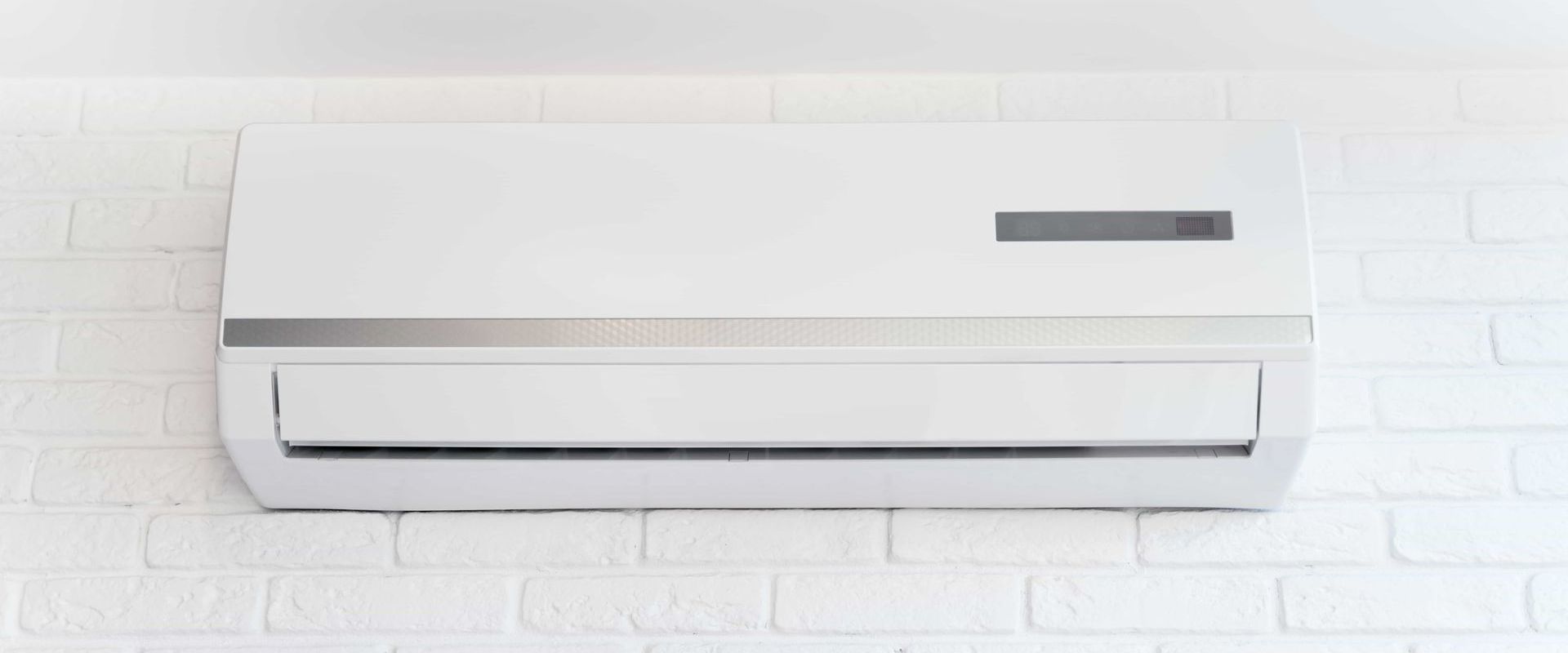 White air conditioner mounted on a white brick wall.