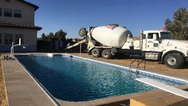 A cement truck is pouring concrete around a swimming pool.