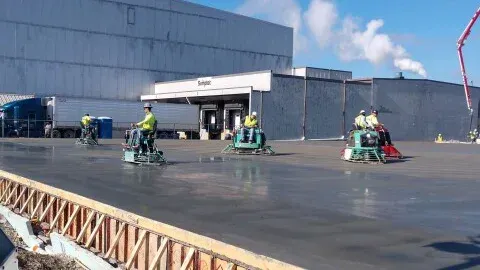 A group of construction workers are working on a concrete floor in front of a large building.