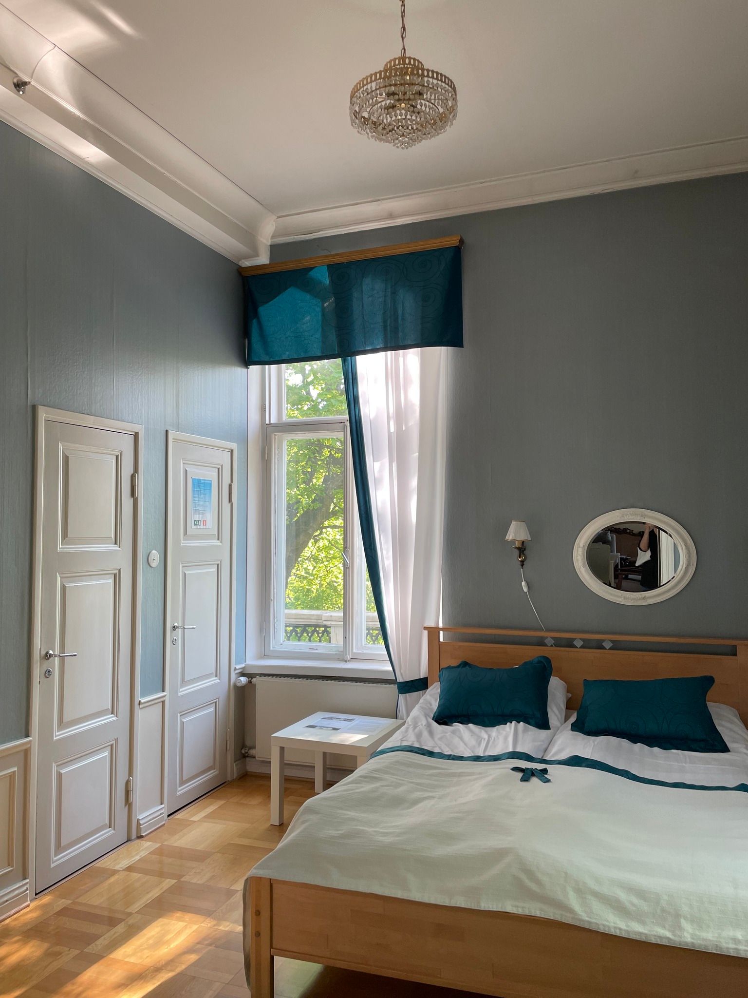 A bedroom with a bed , curtains , a mirror and a window.
