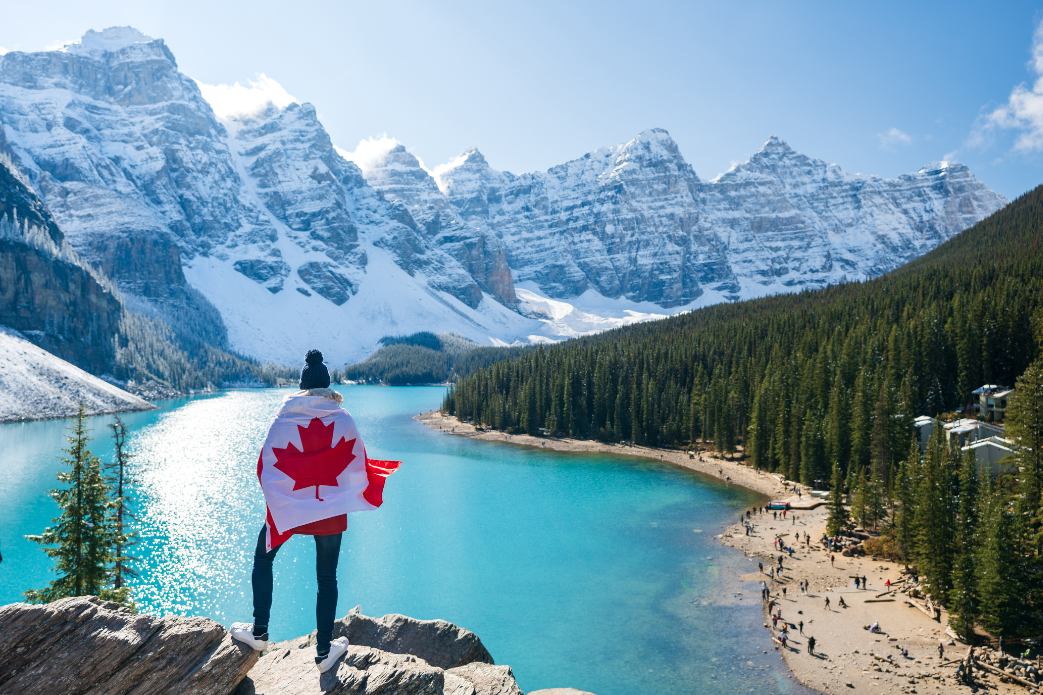 Una persona está parada en la cima de una montaña sosteniendo una bandera canadiense.