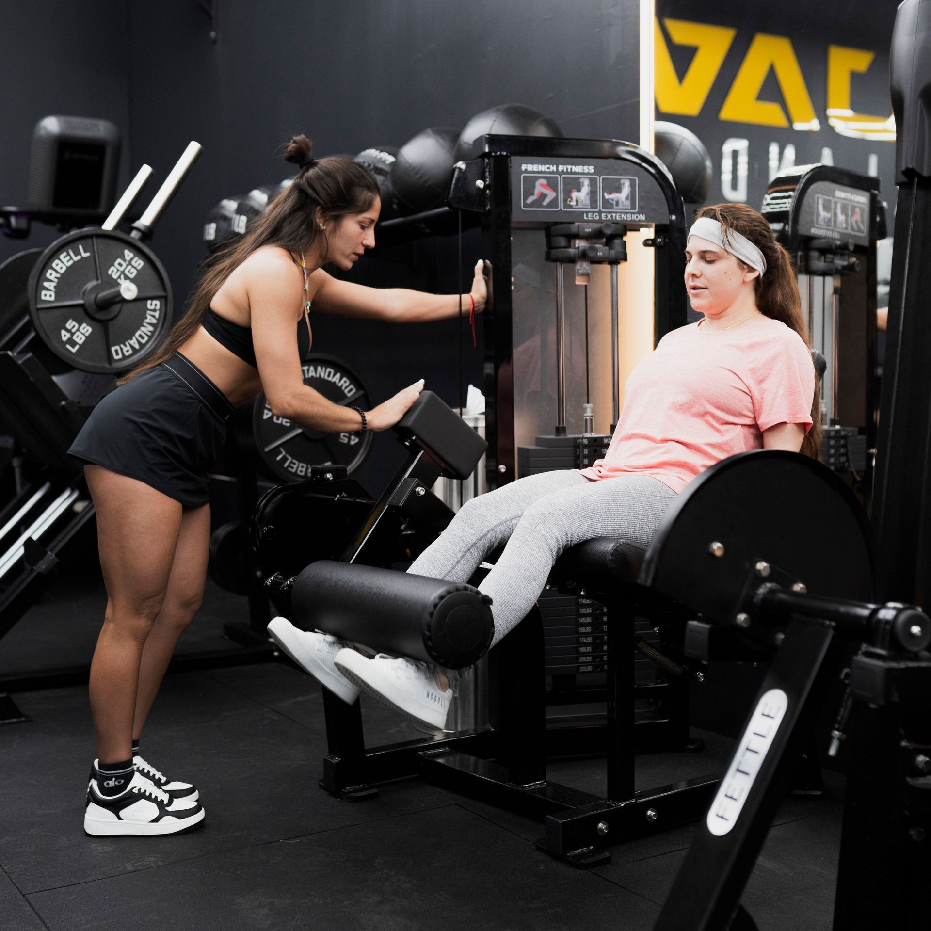 A man is helping a woman do leg presses in a gym. DEJA VU GYM