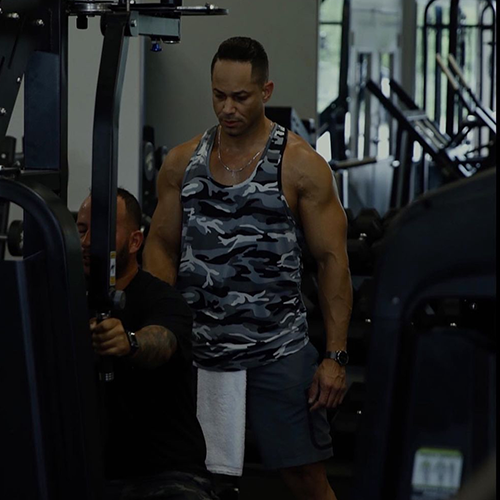 A man in a camo tank top is standing in a gym.