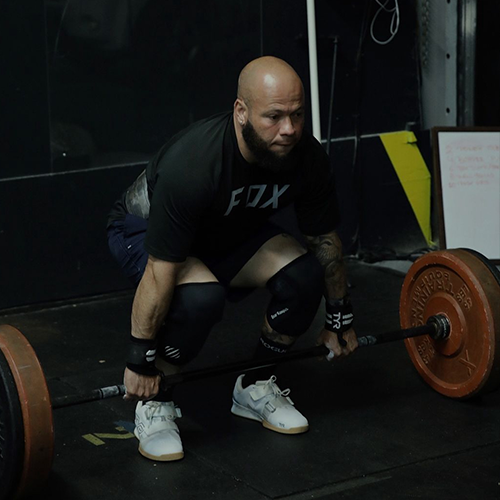 A man squatting down holding a barbell with a fox shirt on