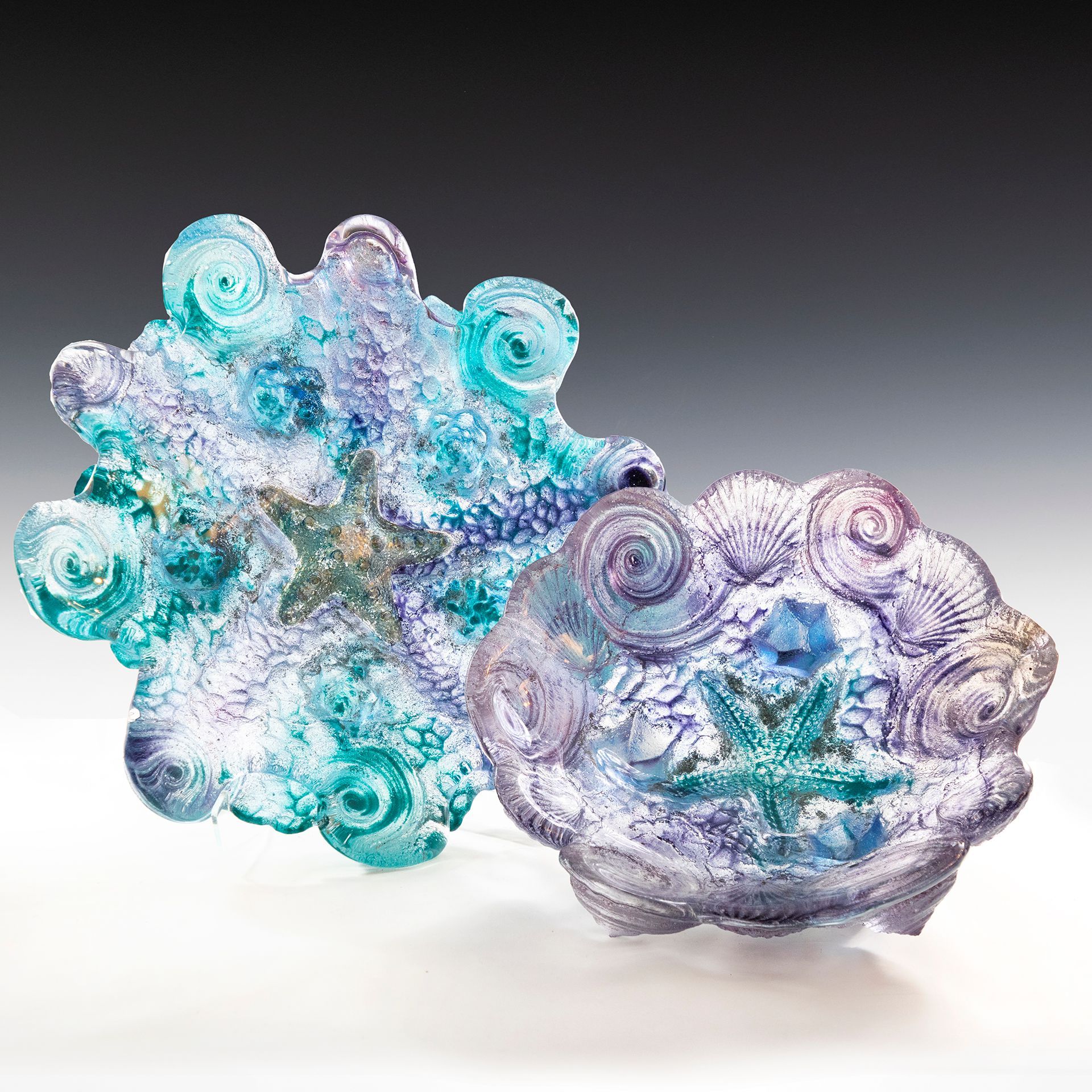 Two glass bowls with seashells on them are sitting on a table.