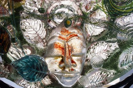 A close up of a glass sculpture with a face and leaves on it.